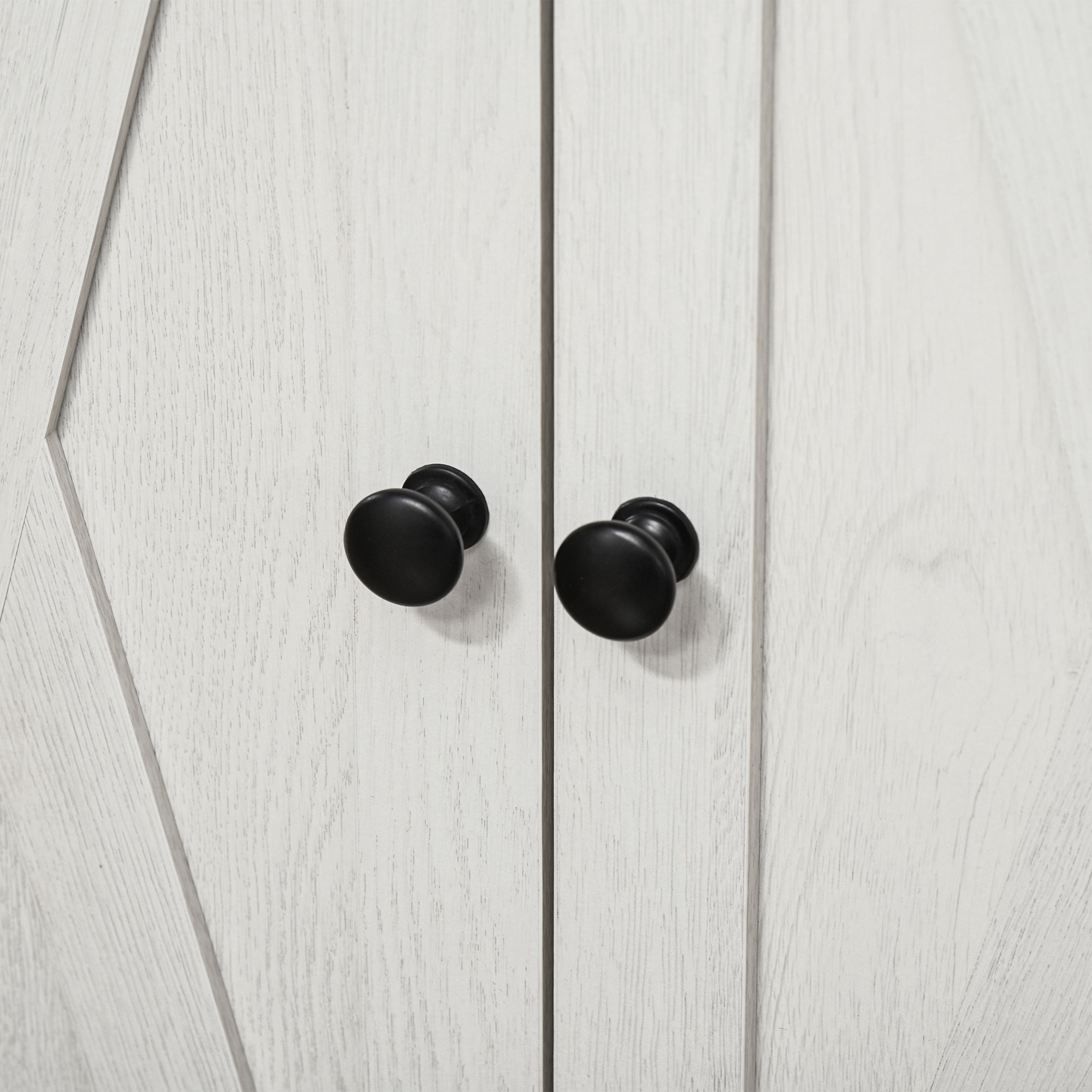 Due pomelli rotondi neri su una superficie in legno chiaro con scanalature verticali.