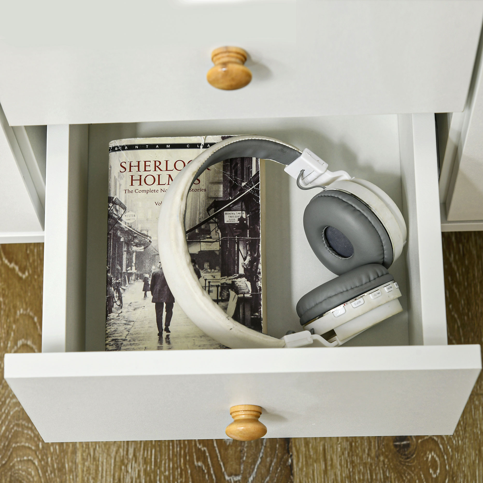 Cuffie bianche appoggiate su un libro di Sherlock Holmes in un cassetto.