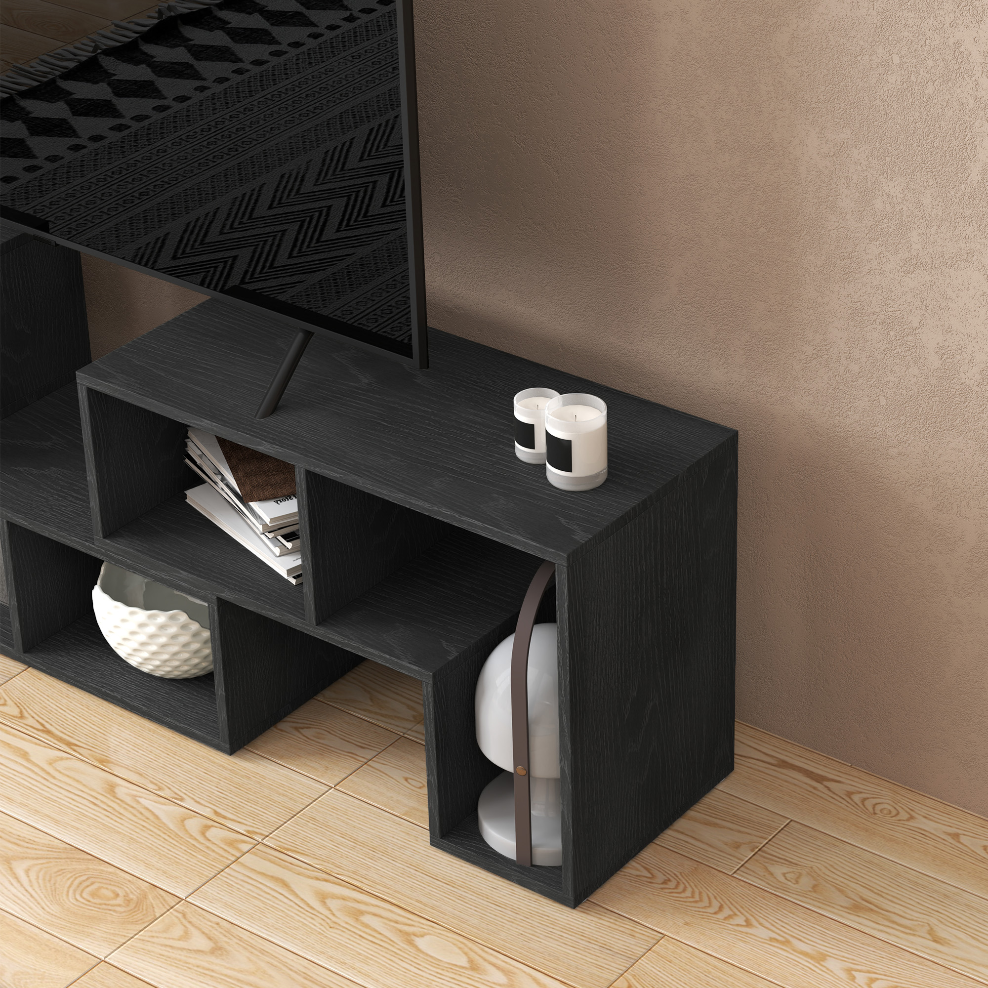 Una mensola nera con libri, candele e oggetti decorativi su pavimento in legno.
