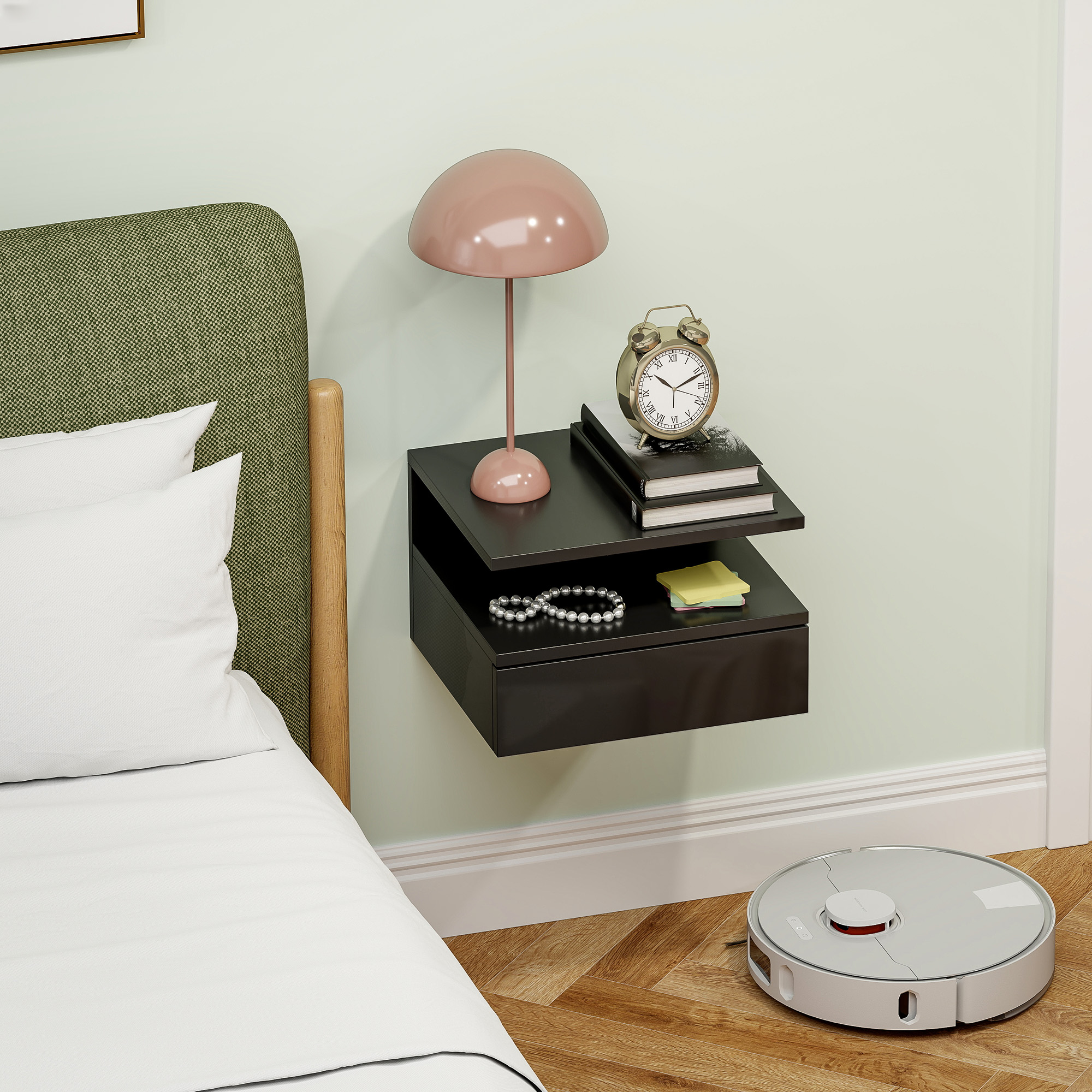 Un comodino con lampada, sveglia e libri accanto a un letto, con un robot aspirapolvere a terra.