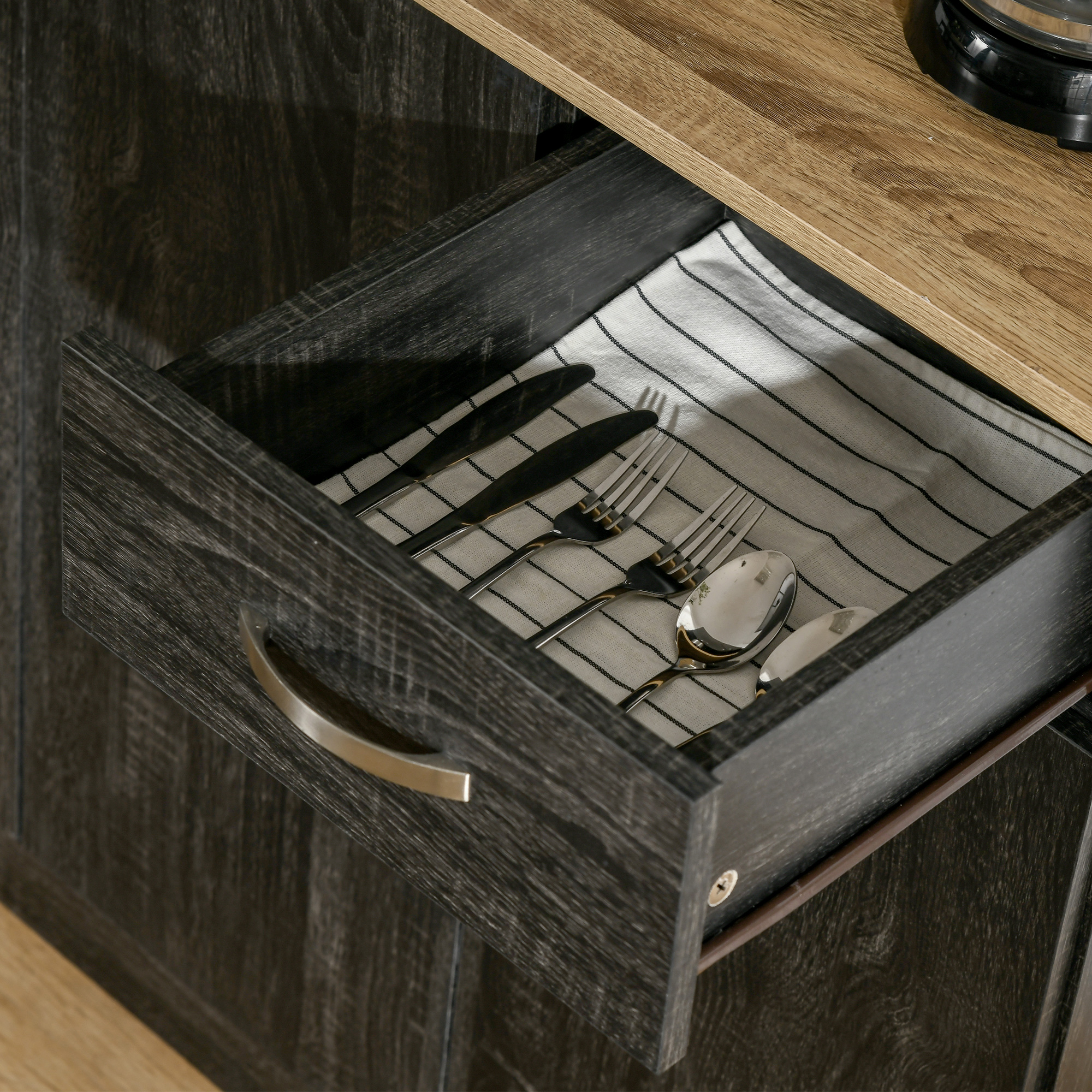 Un cassetto di legno aperto con posate su un panno a righe.