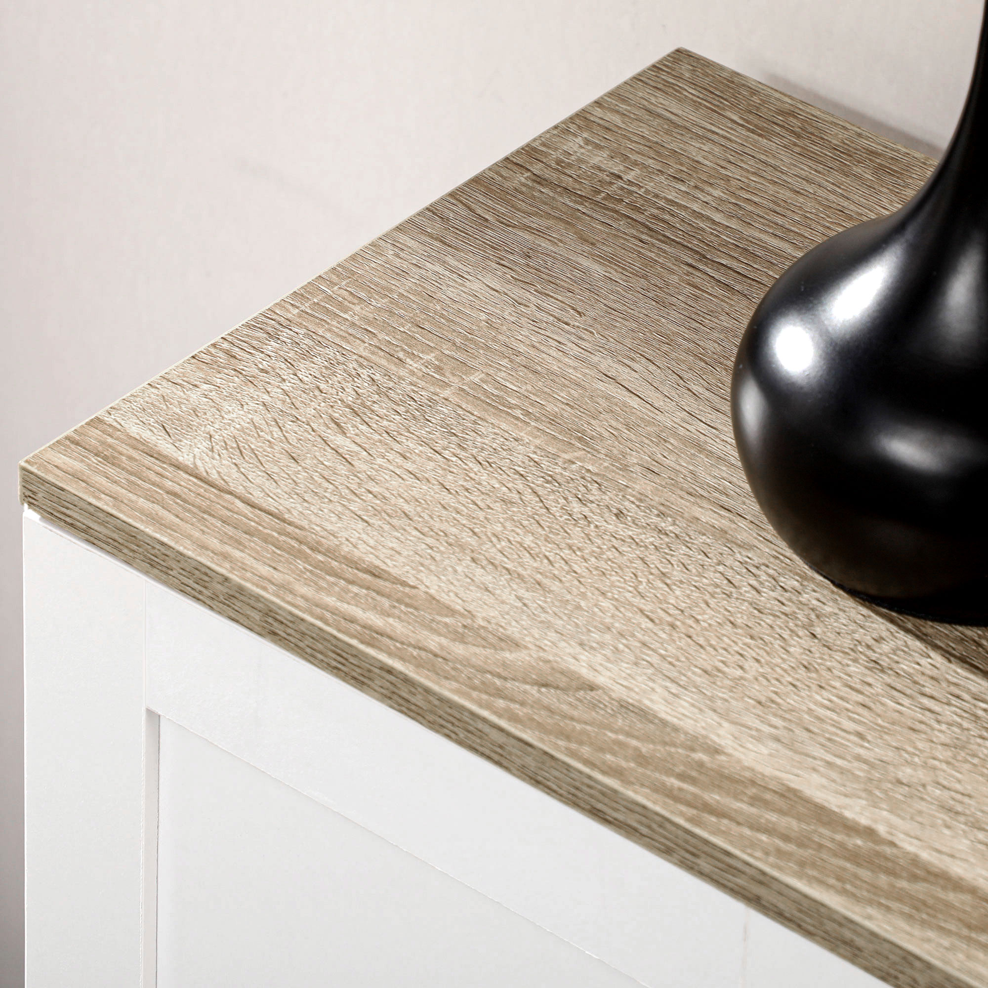 Un vaso nero su un mobile in legno chiaro con cassetti bianchi.
