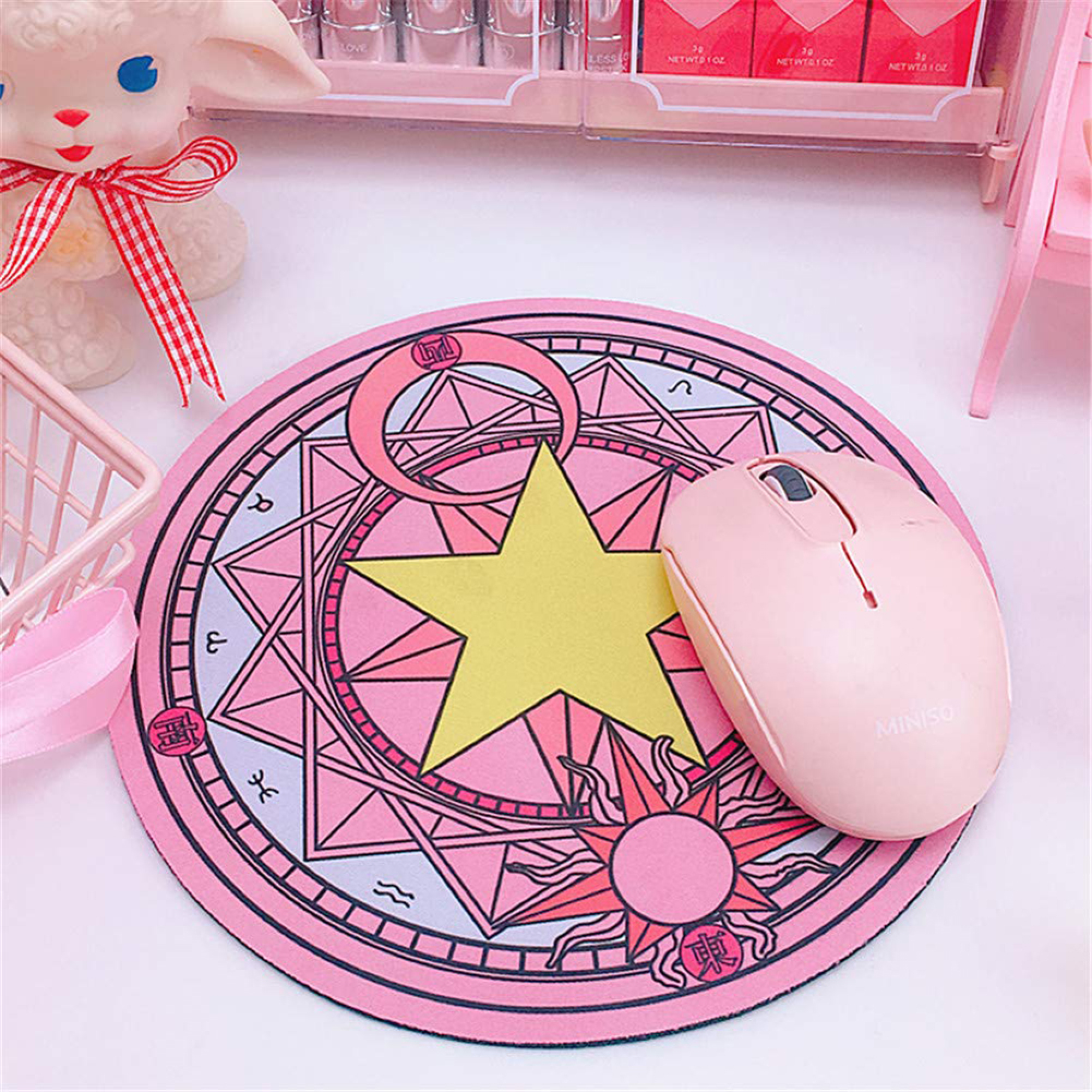 Eine rosa Maus liegt auf einem runden rosa Mousepad mit Sternen und Sonnensymbolen.