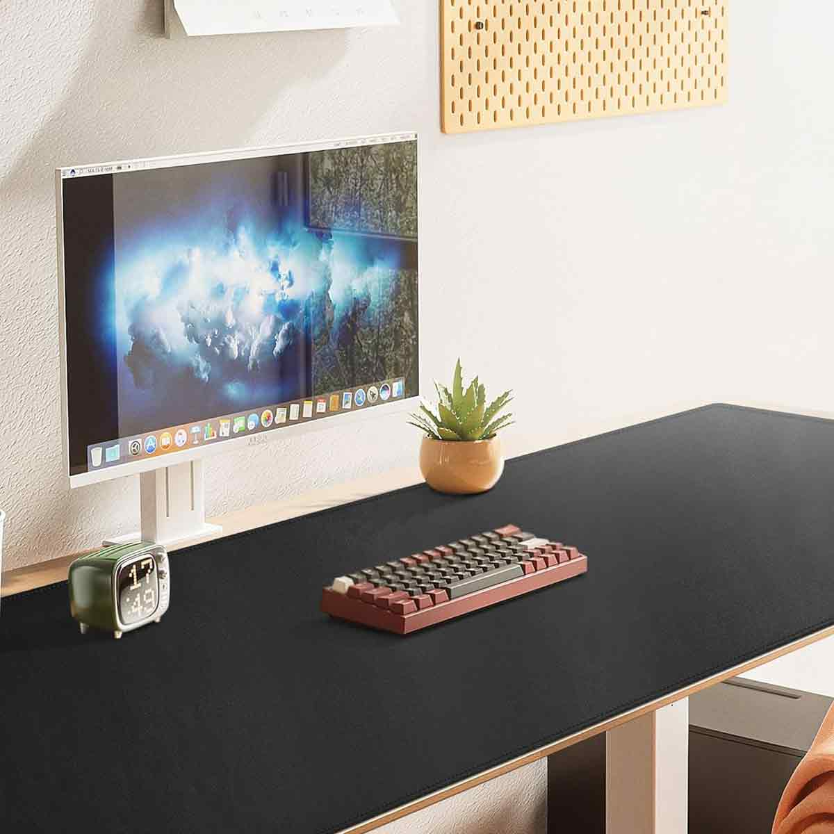 Schreibtisch mit Monitor, Tastatur, Uhr und Pflanze.