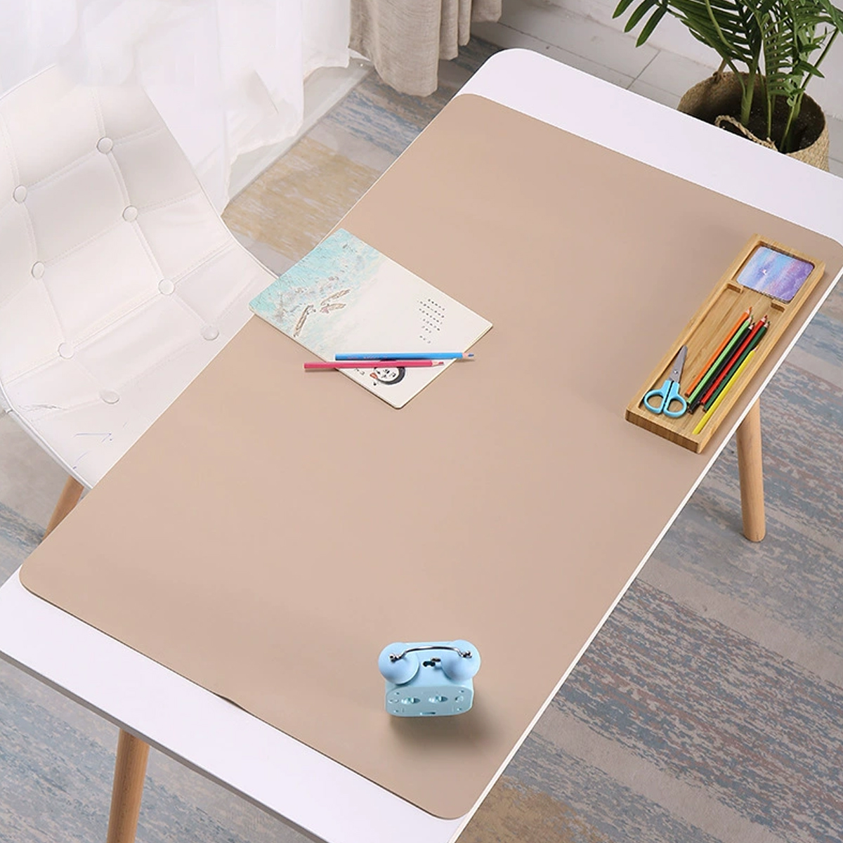 Ein Schreibtisch mit einer beigen Matte, Stiften, Schere, Notizbuch und einem blauen Hefter.
