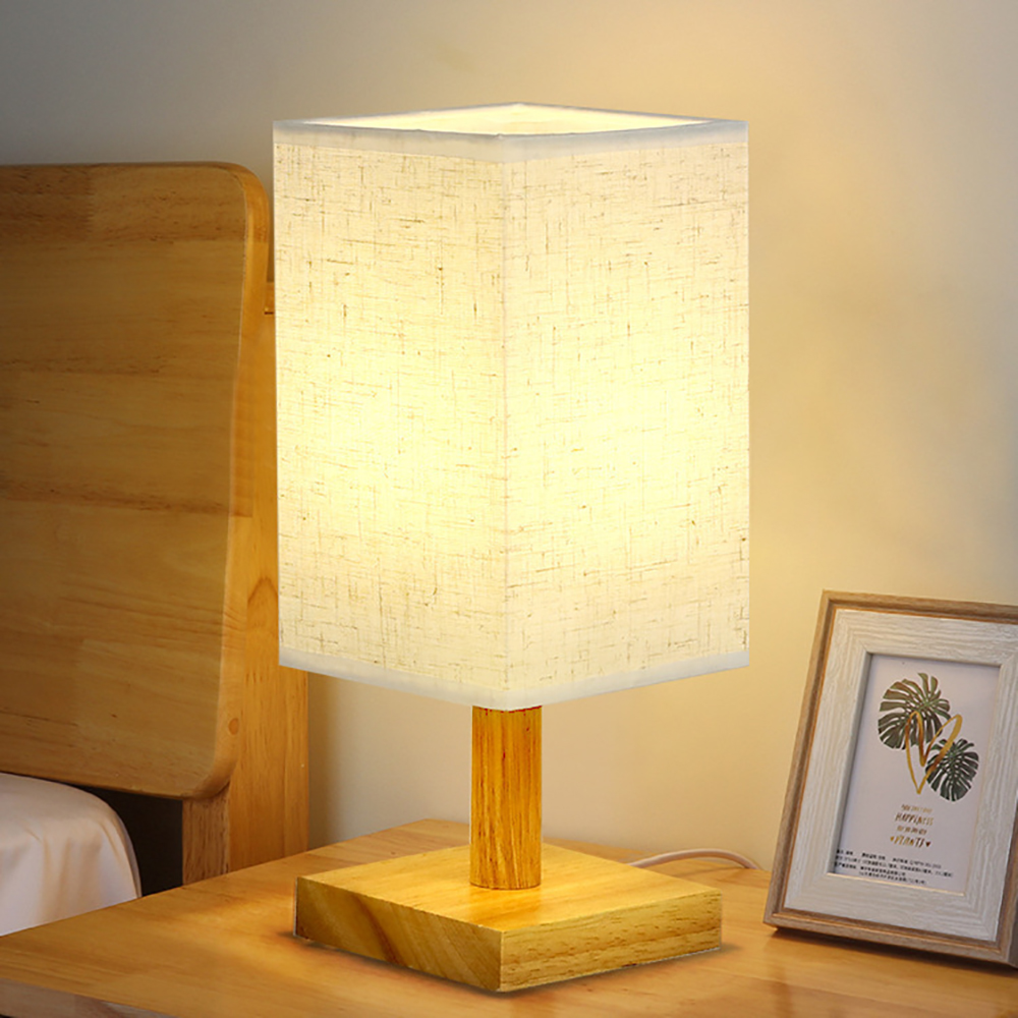 Eine Nachttischlampe mit Stoffschirm steht auf einem Holztisch neben einem Bett.