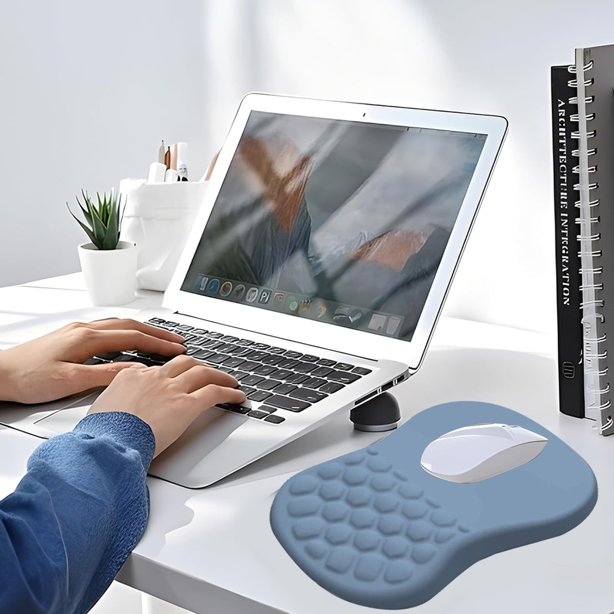 Person tippt auf Laptop, Maus auf blauem Handgelenkauflage daneben.