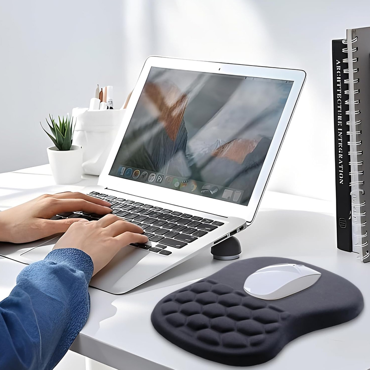Person tippt auf Laptop, Maus auf Handballenauflage, Schreibtisch mit Büromaterial.