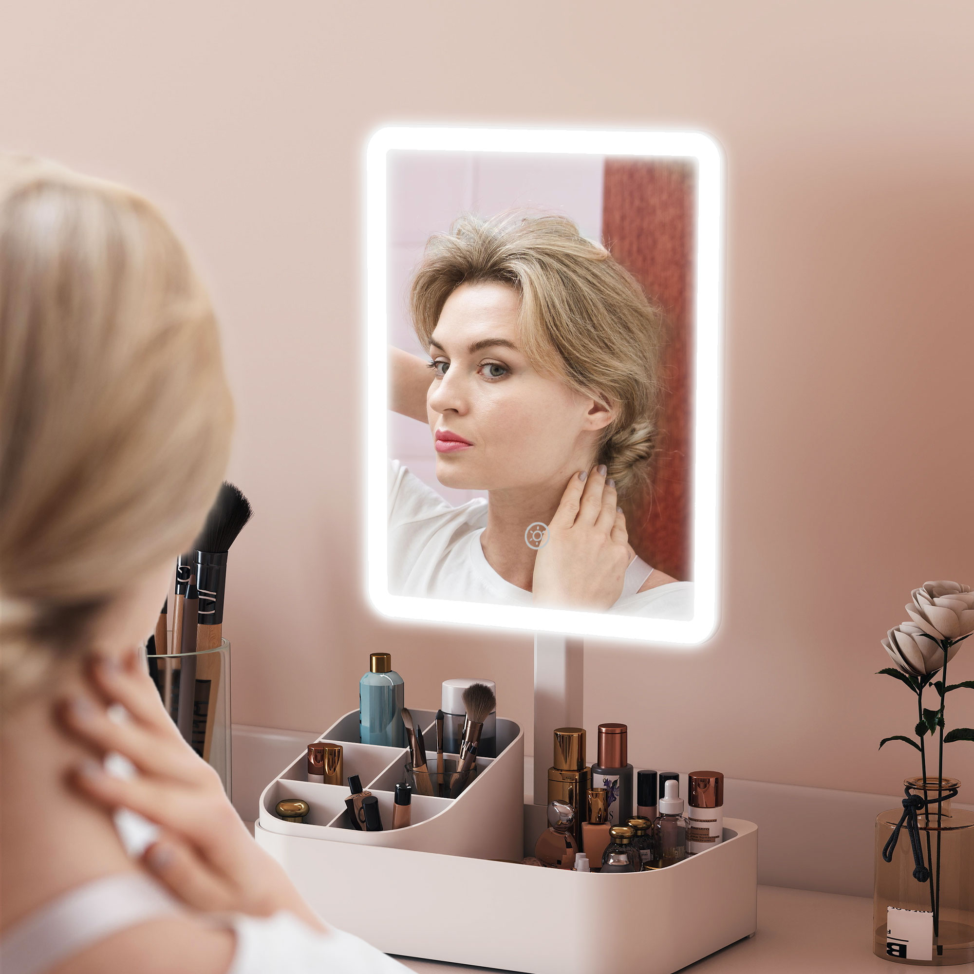 Donna si sistema i capelli allo specchio illuminato. Organizer makeup su toeletta.