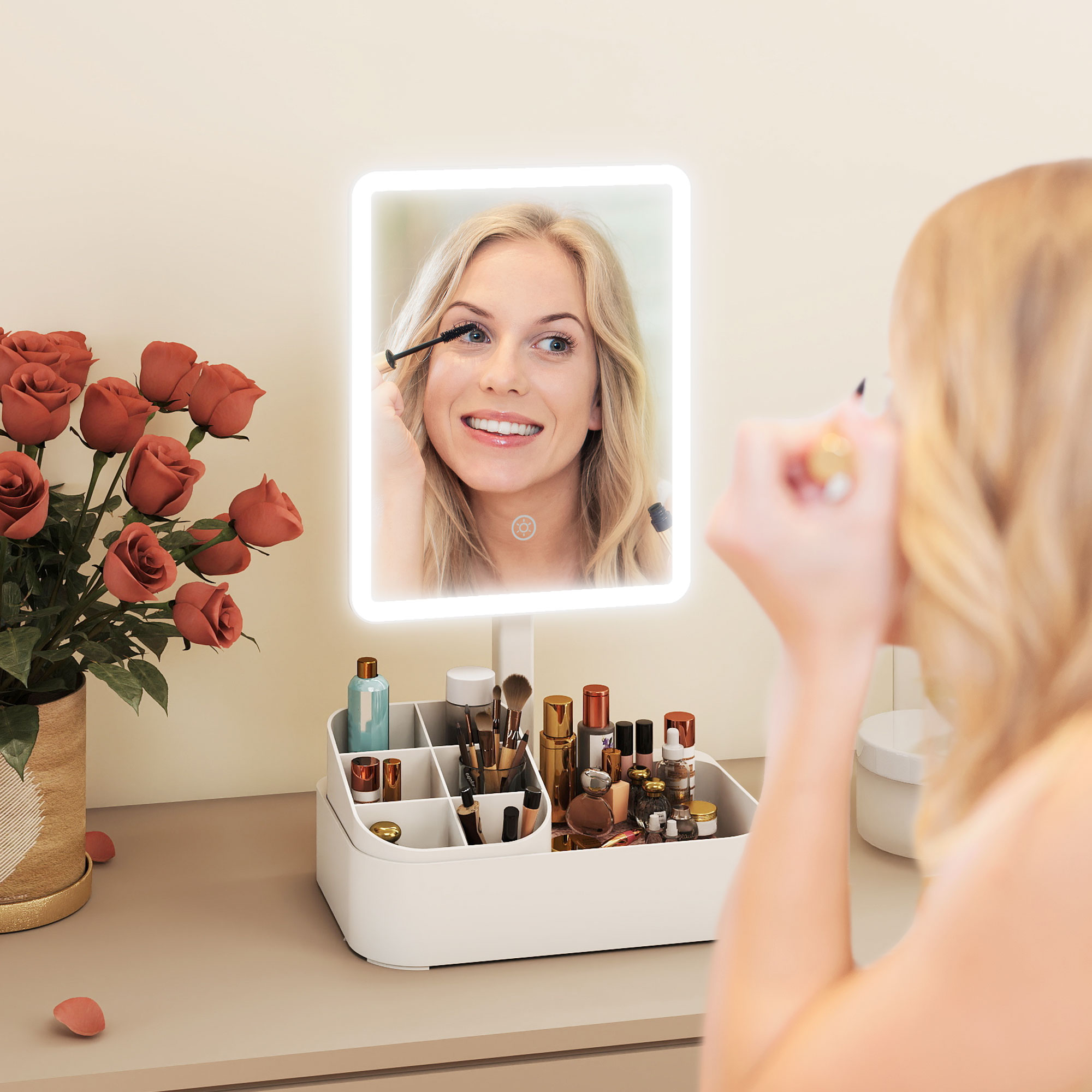 Una donna si applica il mascara in uno specchio illuminato, vicino a rose e cosmetici.
