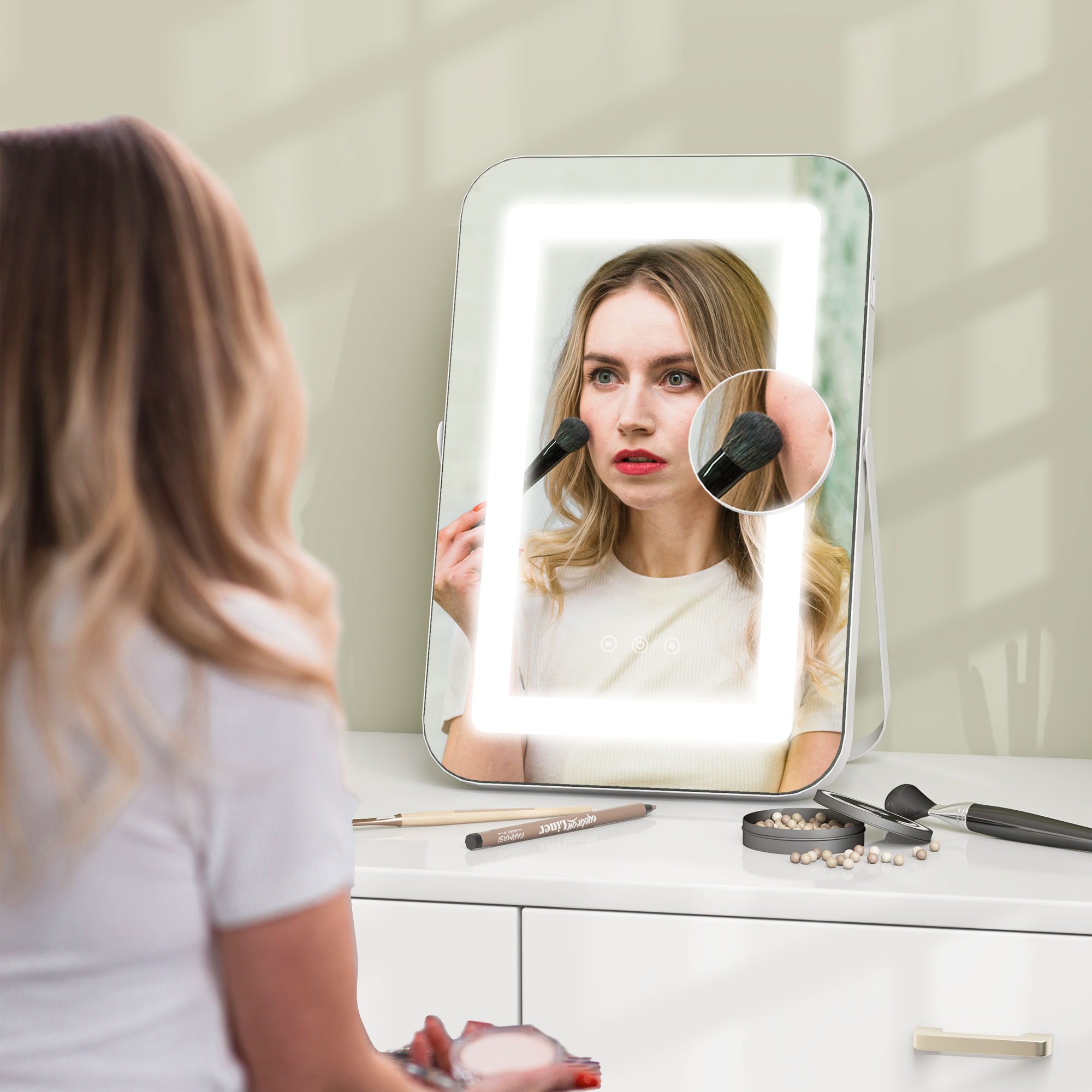 Una donna si trucca davanti a uno specchio da toeletta illuminato. Cosmetici su un comò bianco.