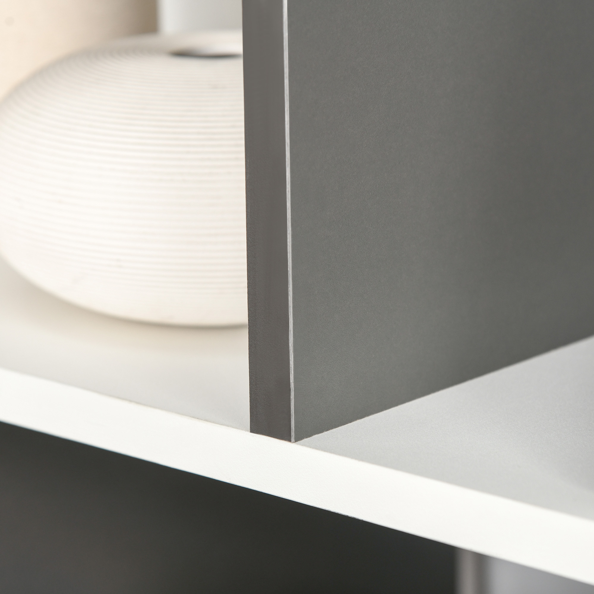 Un vaso bianco scanalato si trova su uno scaffale accanto a un pannello grigio.
