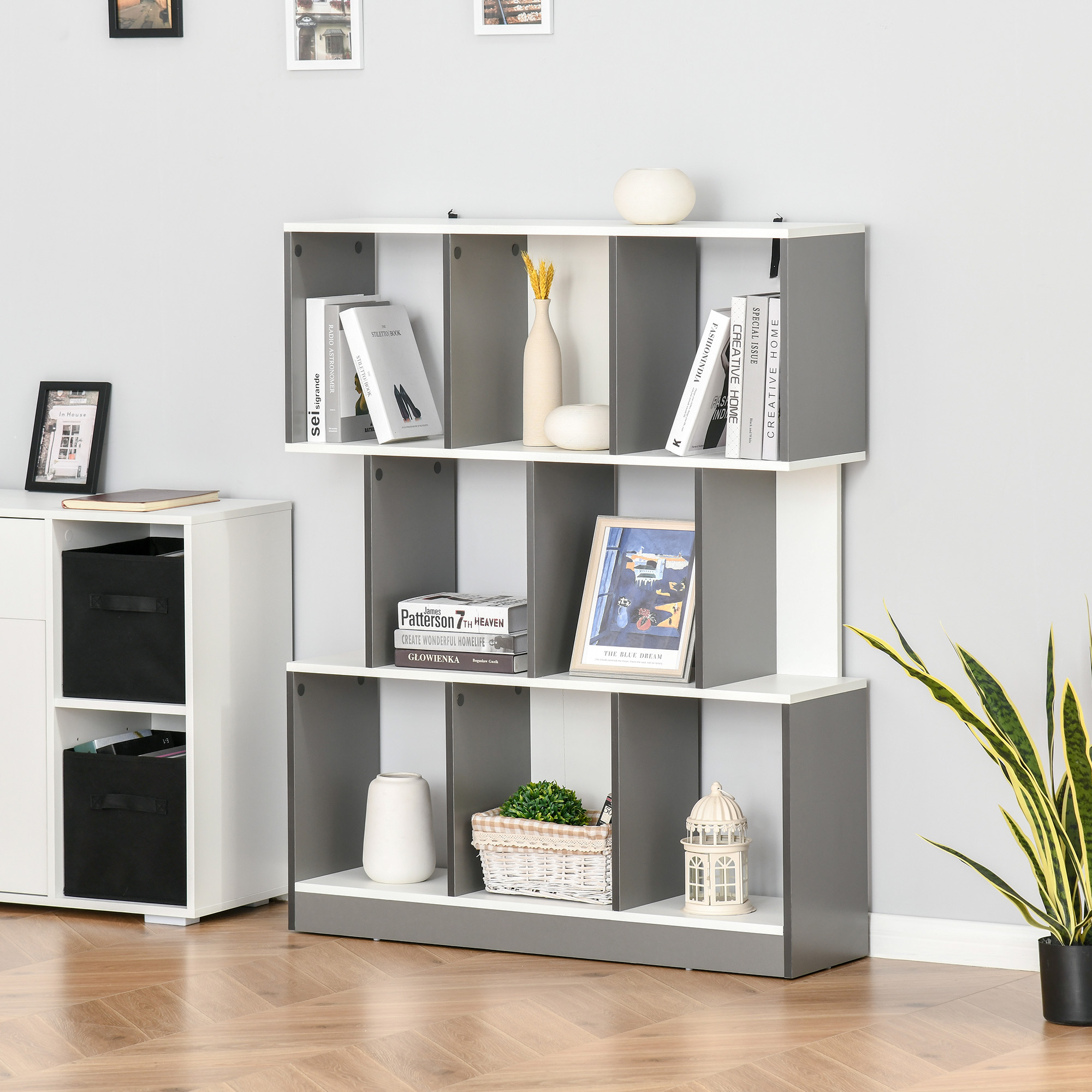 Una libreria grigia e bianca espone libri, vasi, un quadro incorniciato e contenitori.