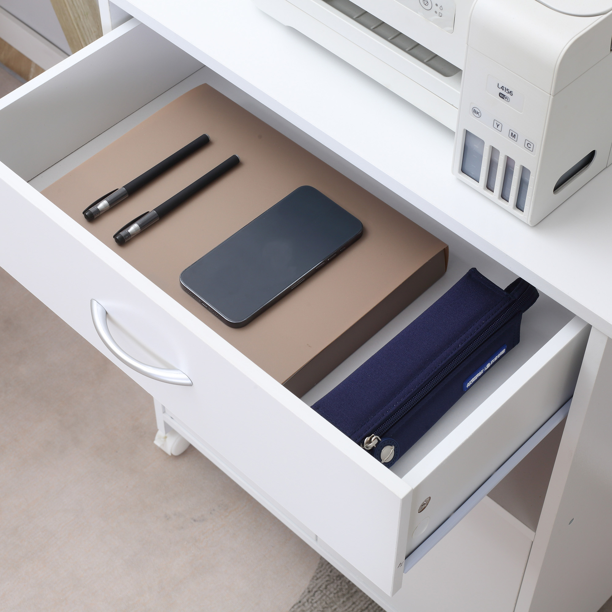Un organizer da cassetto bianco aperto con penne, uno smartphone e un astuccio blu scuro.