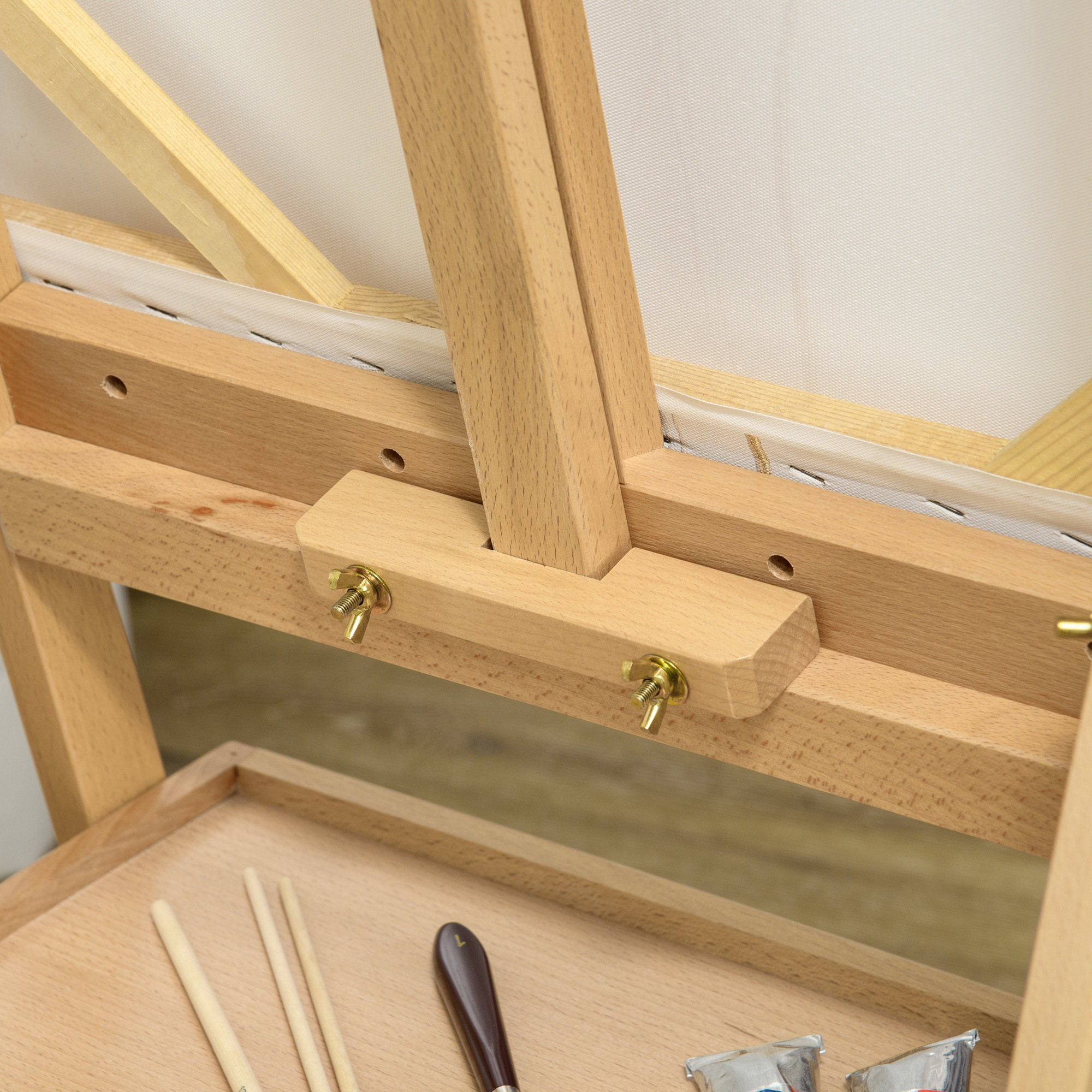 Telaio da cavalletto in legno con tela. Pennelli e tubetti di vernice sotto.