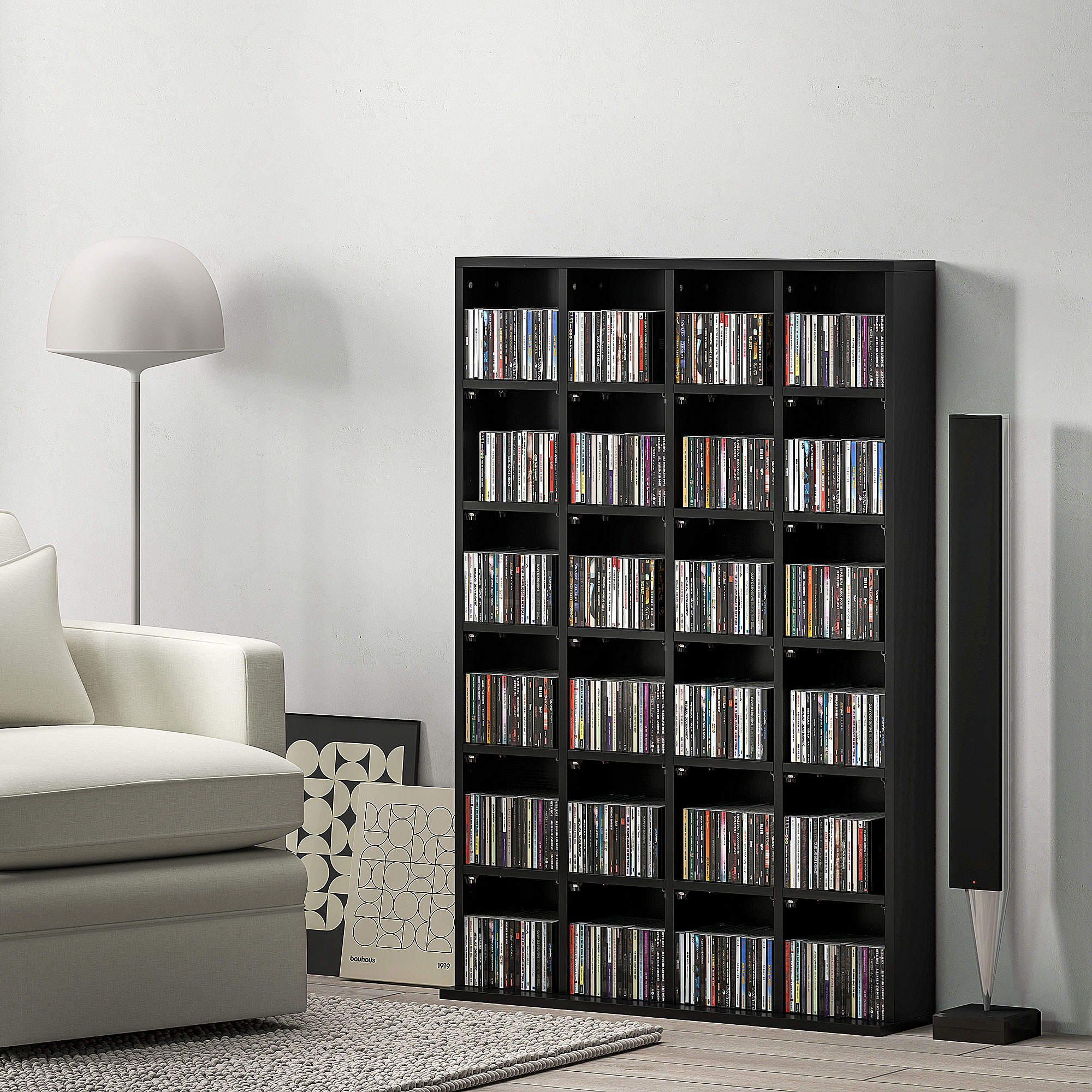 Una scaffalatura nera piena di CD, accanto a un divano, lampada e altoparlanti.