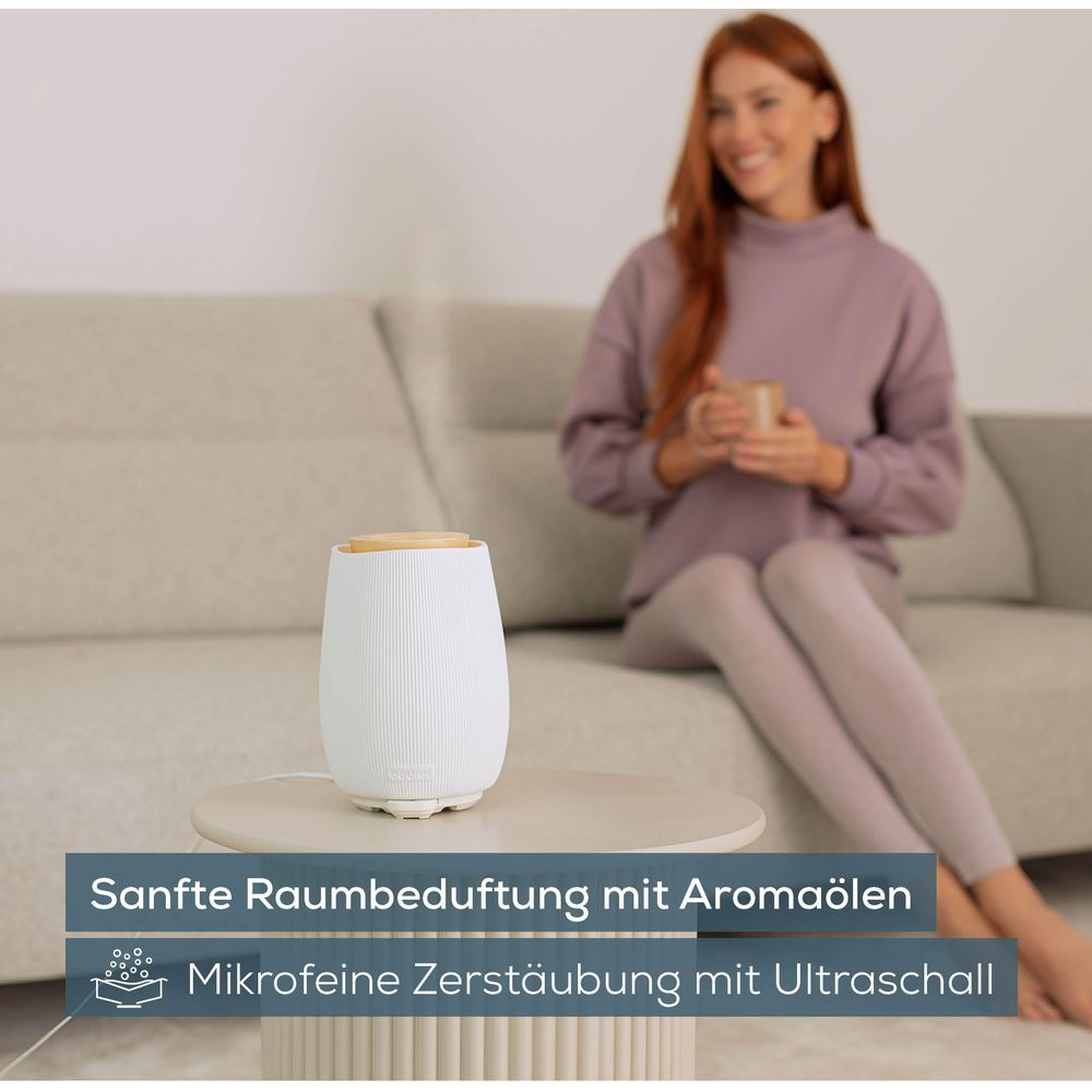 Eine Frau sitzt auf einem Sofa und trinkt aus einer Tasse, daneben ein Diffusor.