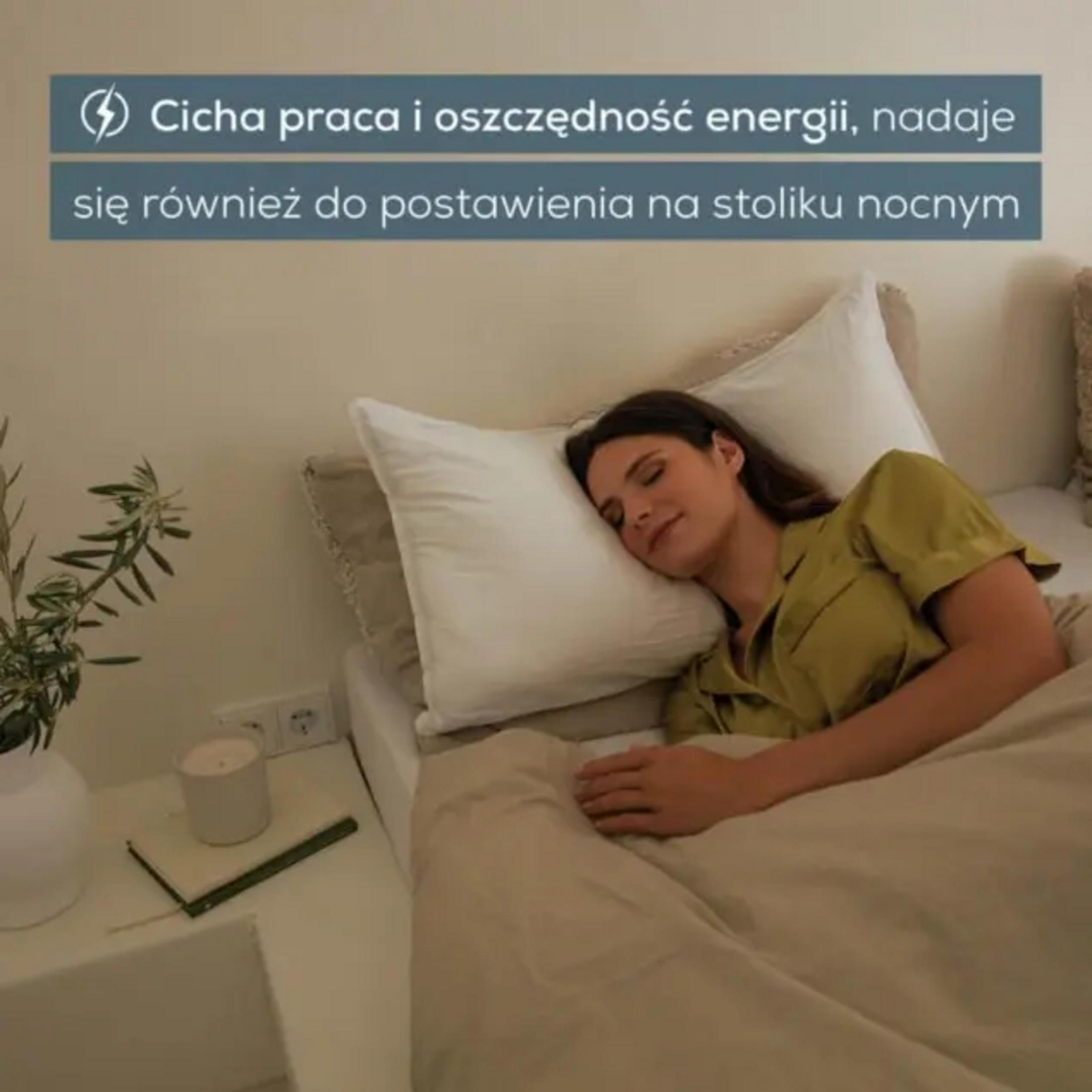 Eine Frau schläft in einem Bett, neben einem Nachttisch mit einer Kerze und einer Pflanze.