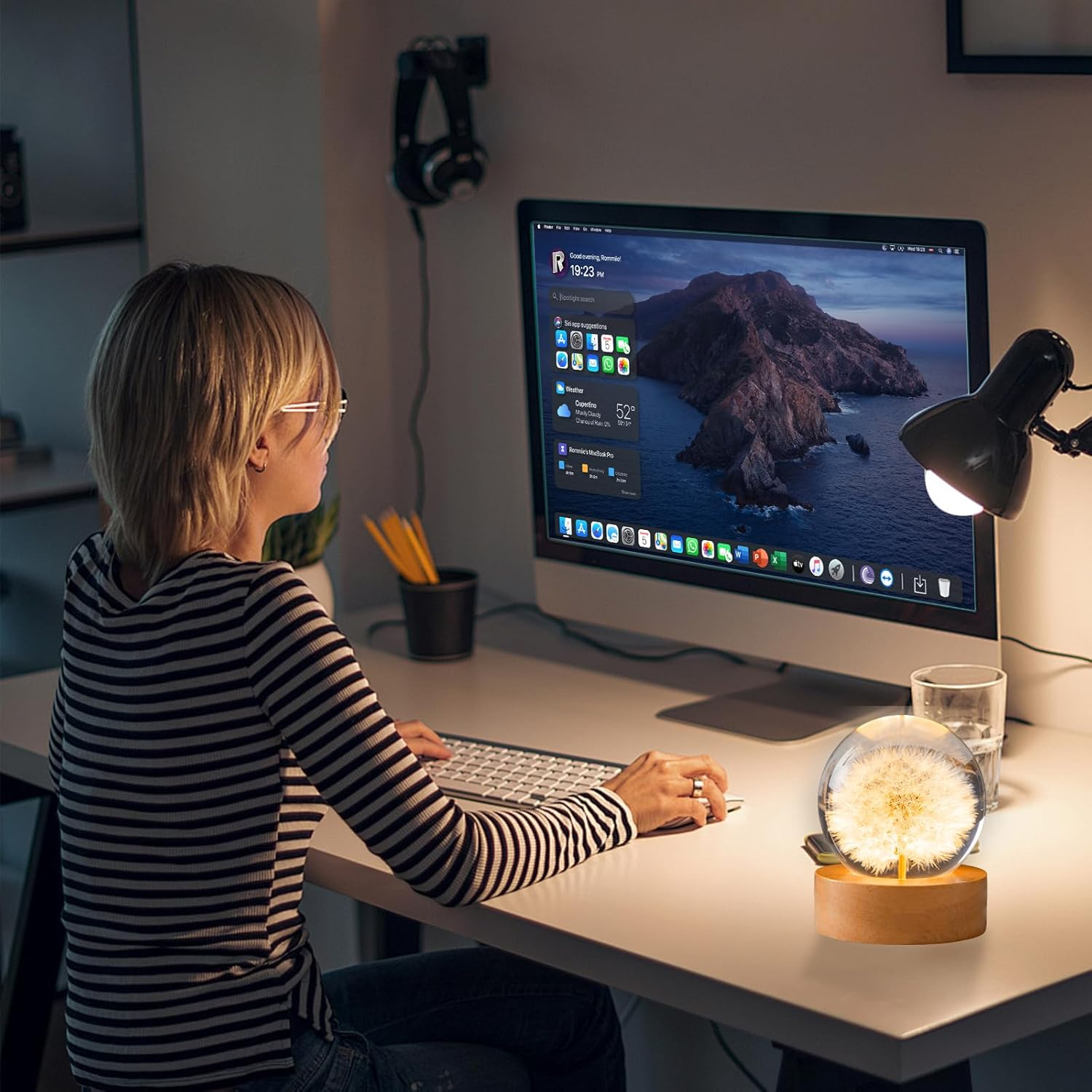 Eine Frau tippt auf einer Tastatur vor einem leuchtenden Computermonitor mit einer Löwenzahnlampe.