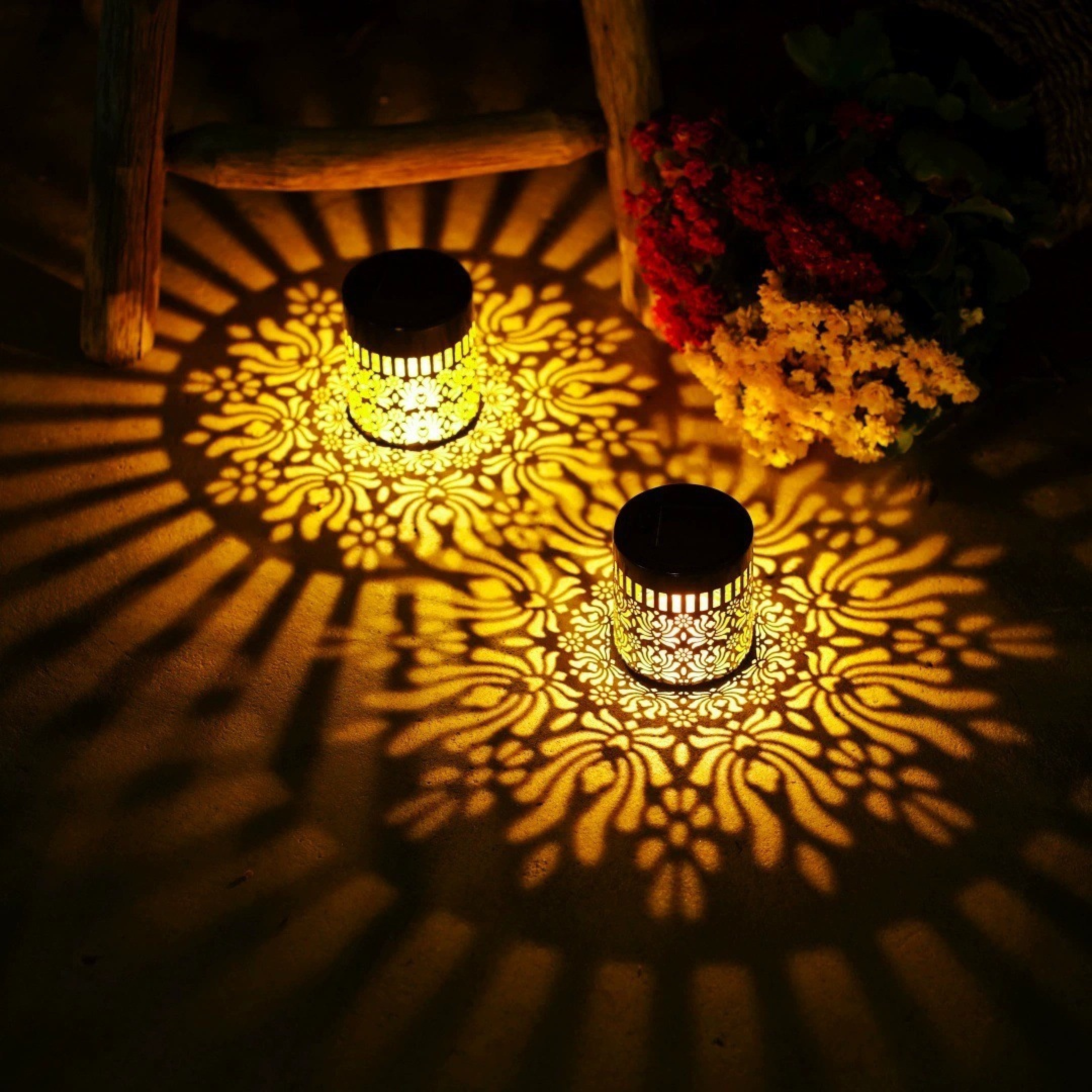 Zwei Solar-Laternen werfen kunstvolle florale Schatten auf eine strukturierte Oberfläche.