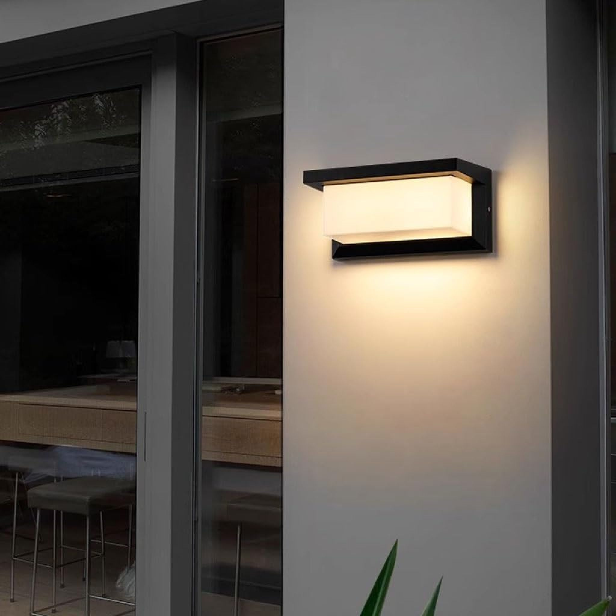 Eine moderne Wandleuchte mit schwarzem Rahmen und Milchglas leuchtet auf einer grauen Wand.