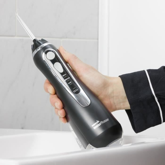 Eine Hand hält einen schwarzen Wasserstrahlreiniger über einem weißen Waschbecken.