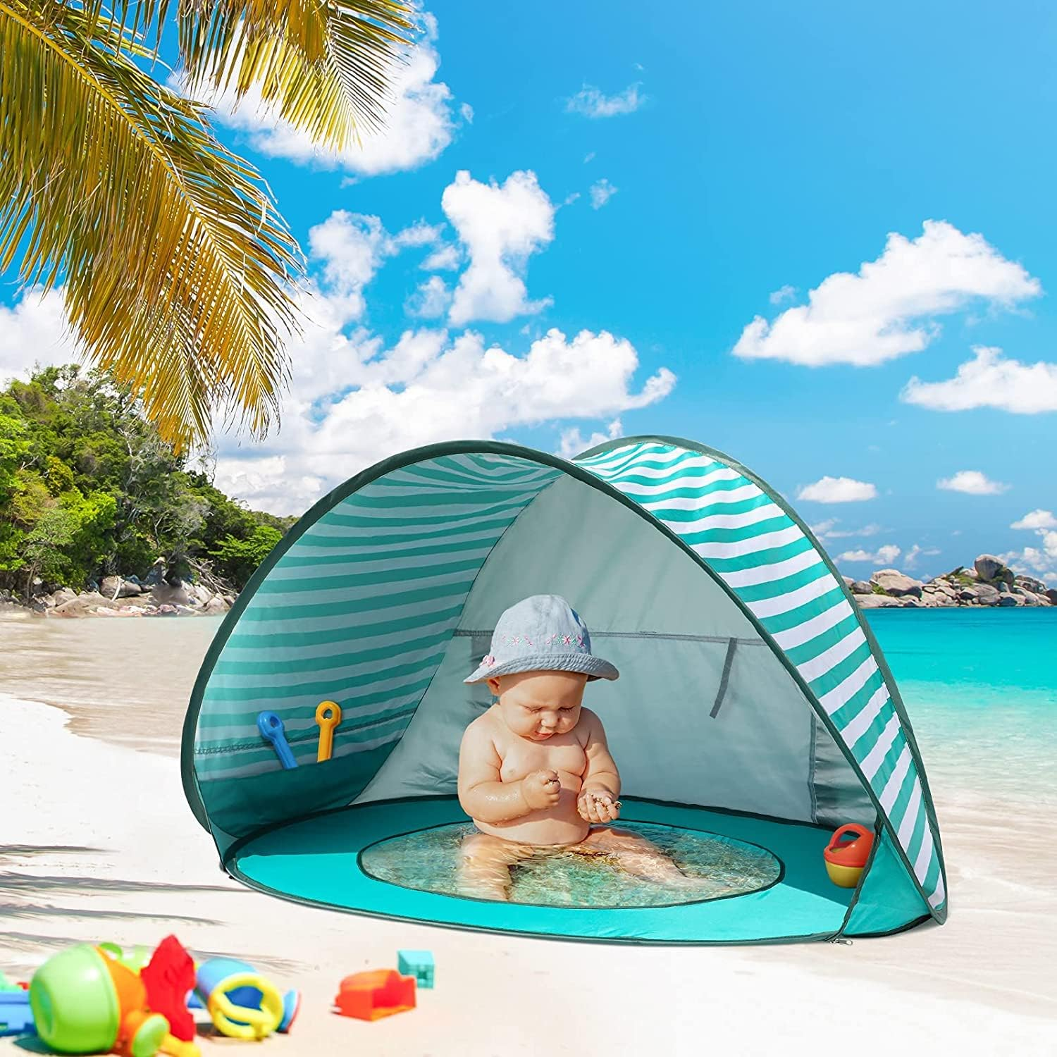 Baby sitzt an einem sonnigen Tag am Meer in einem Strandzelt mit Spielzeug.