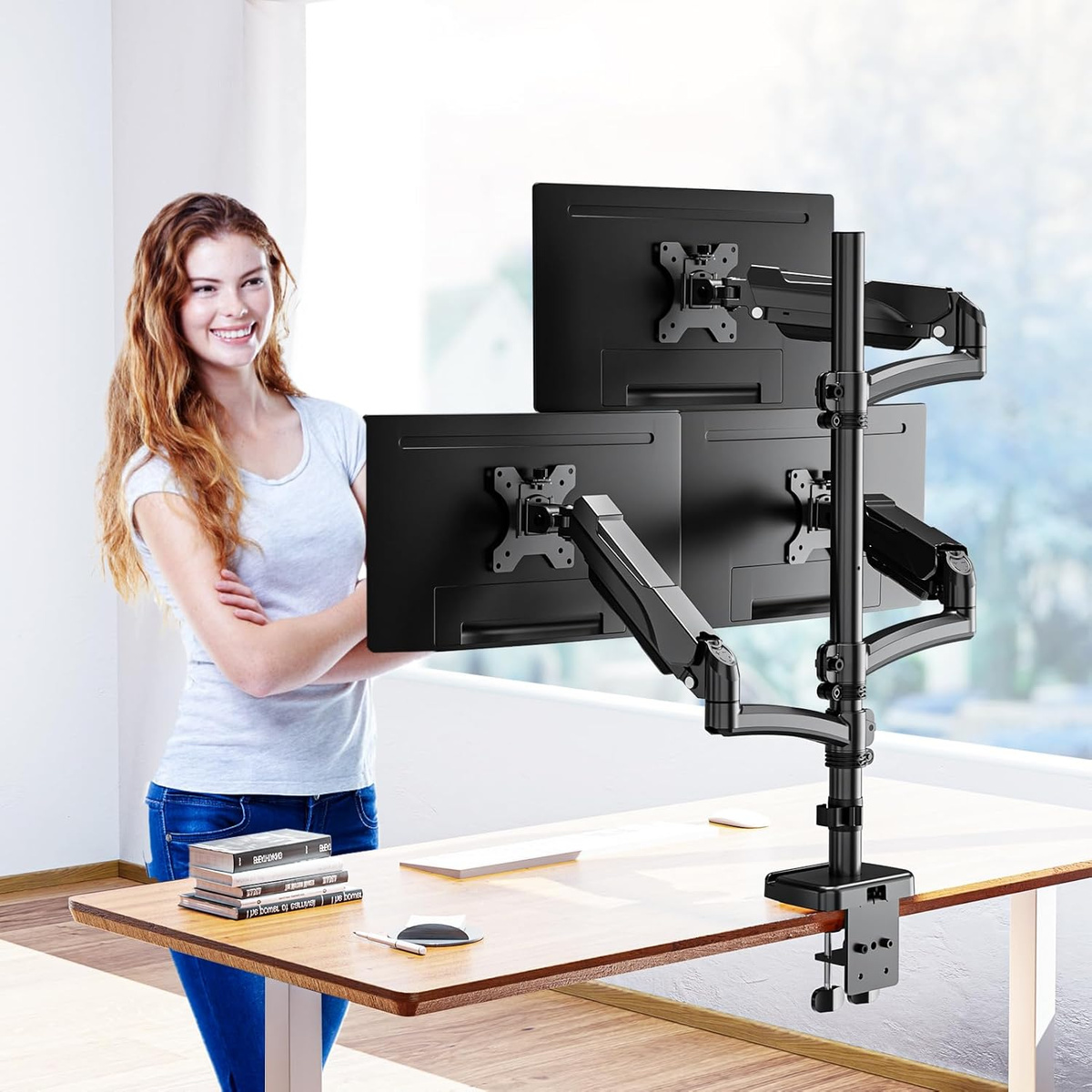 Kobieta obok biurka z potrójnym uchwytem na monitory, na którym zamontowano trzy czarne monitory.