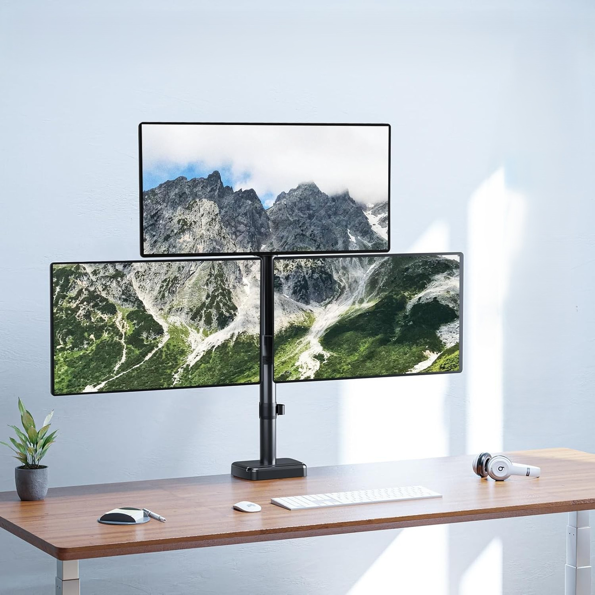Stojak na trzy monitory z krajobrazami górskimi na ekranach.