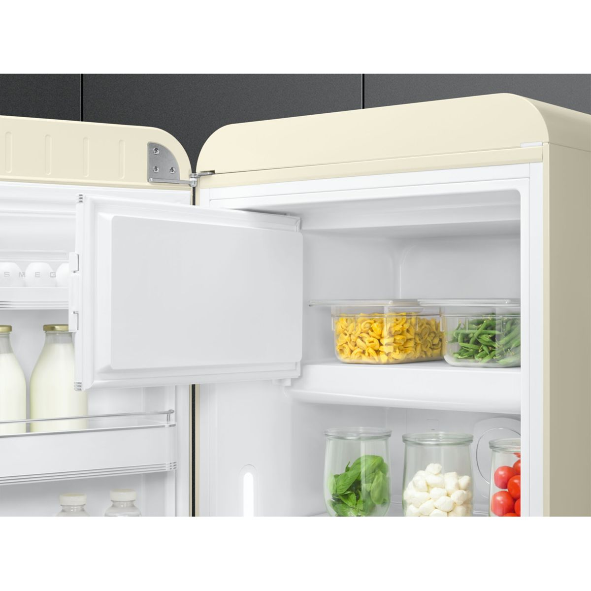 Offener cremefarbener Kühlschrank mit Lebensmitteln: Flaschen, Pasta, Bohnen, Kräuter, Mozzarella und Tomaten.