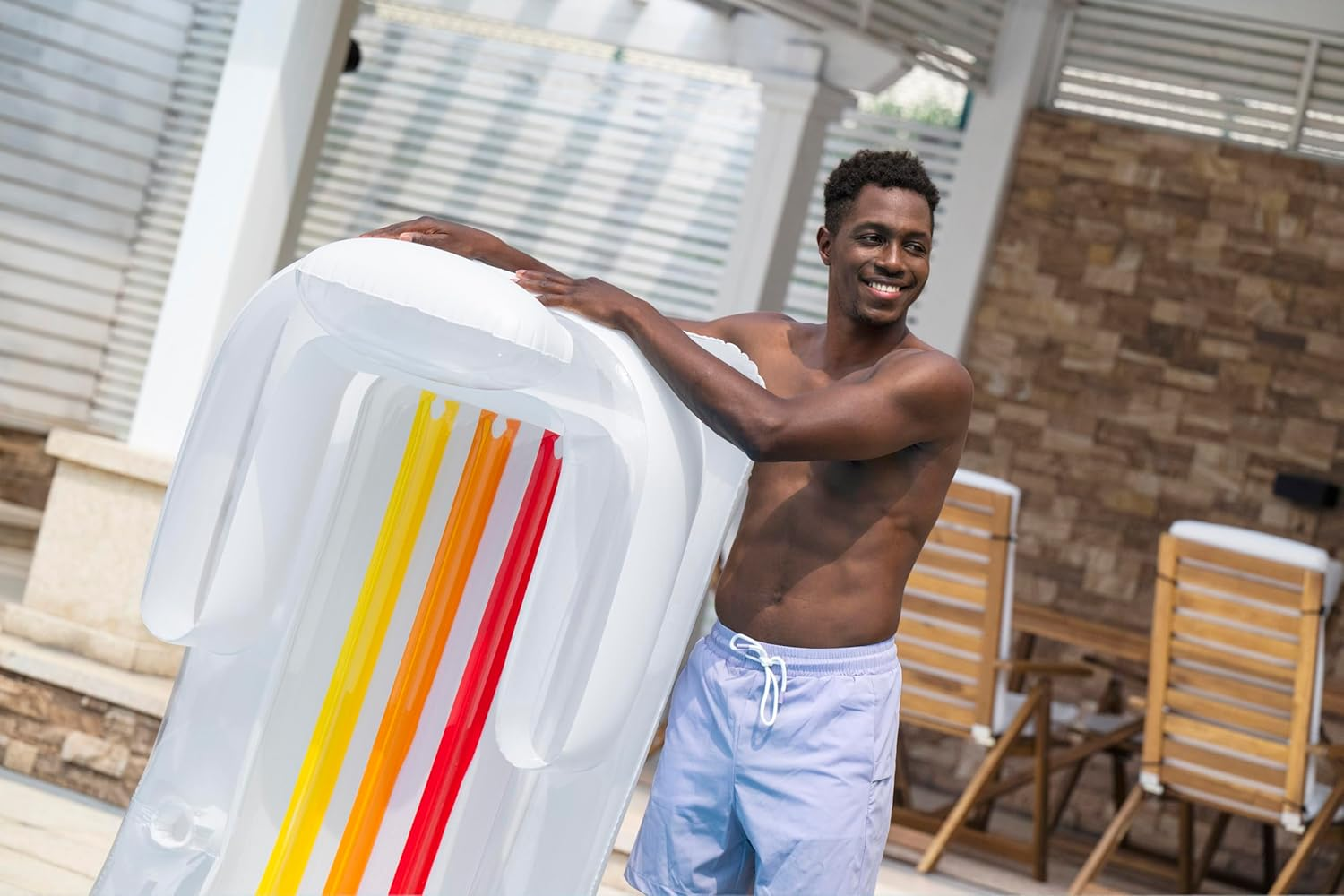 Ein Mann hält eine aufblasbare Luftmatratze mit bunten Streifen am Pool.