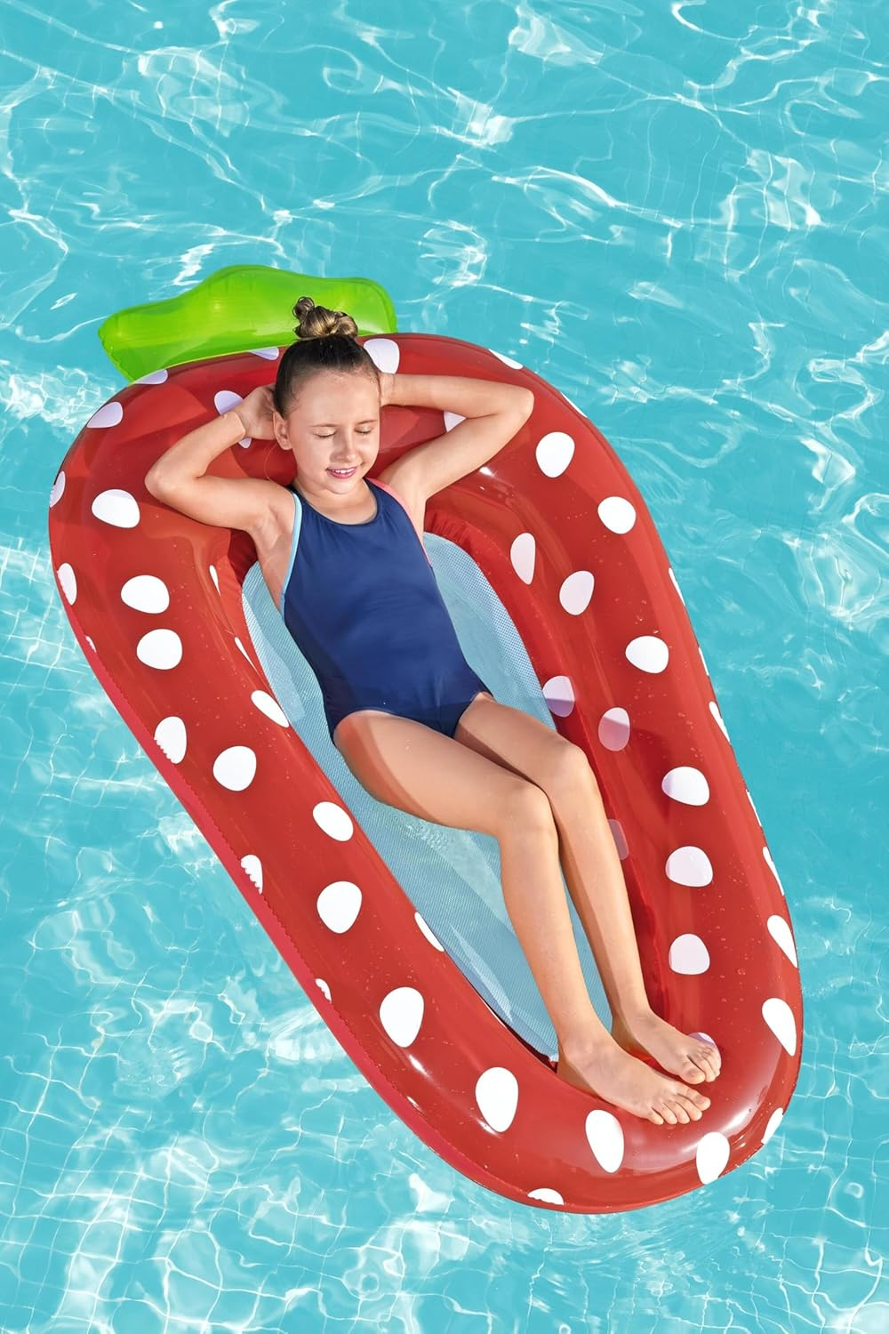 Ein Mädchen entspannt sich auf einer aufblasbaren Erdbeere im Pool.