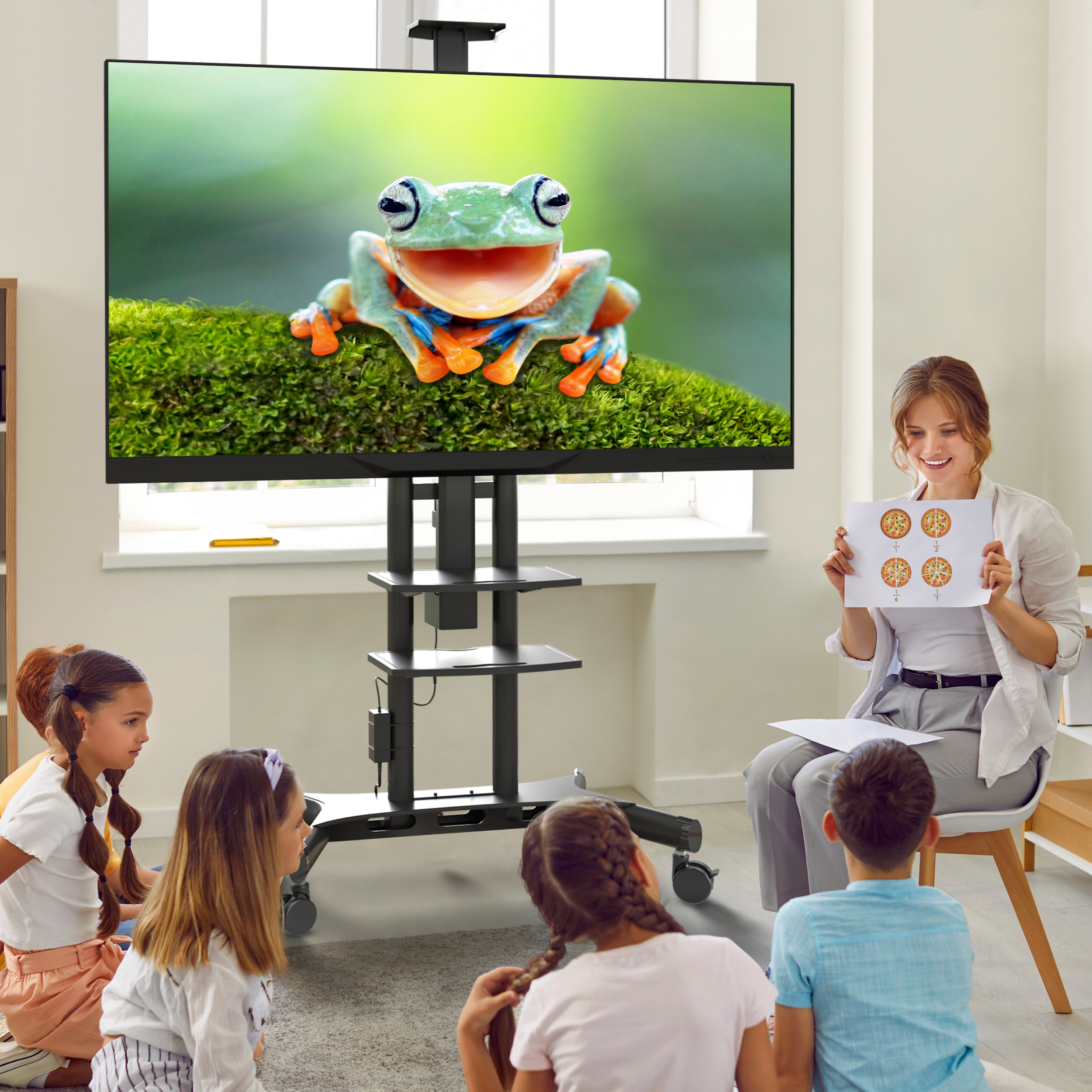 Lehrerin zeigt Kindern eine Abbildung eines Frosches und Pizzen auf einem Bildschirm.