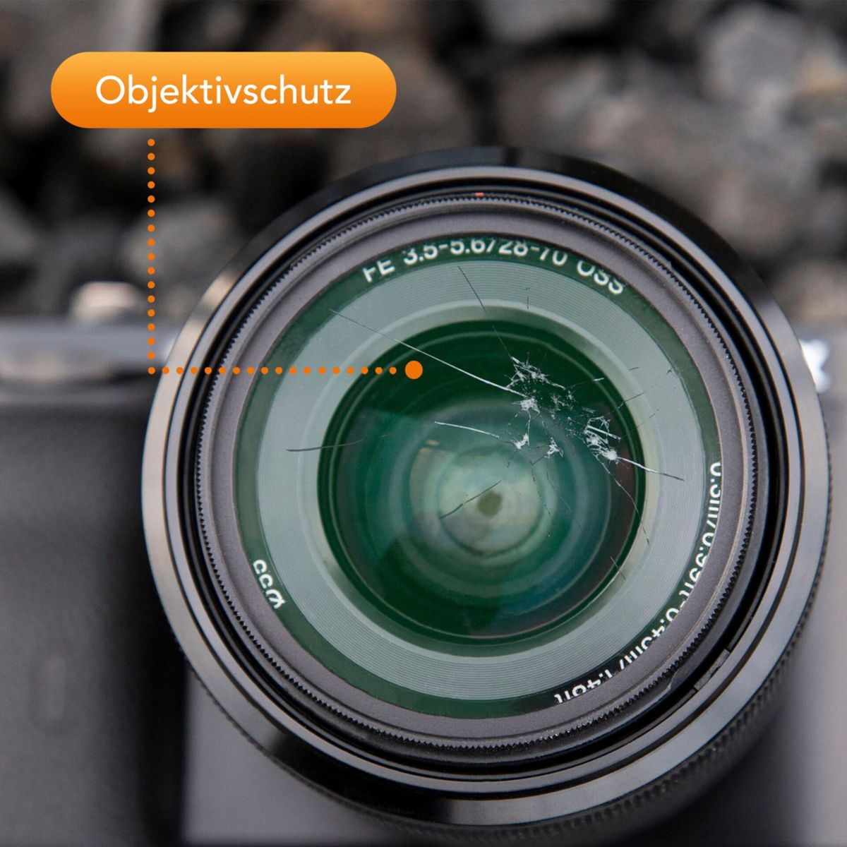 Ein zerbrochenes Kameraobjektiv mit der Aufschrift 'Objektivschutz'.