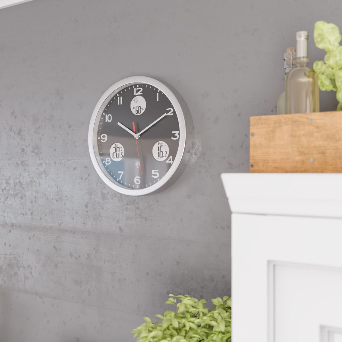 Eine Wanduhr mit silbernem Rahmen zeigt die Zeit und Wetterdaten an.