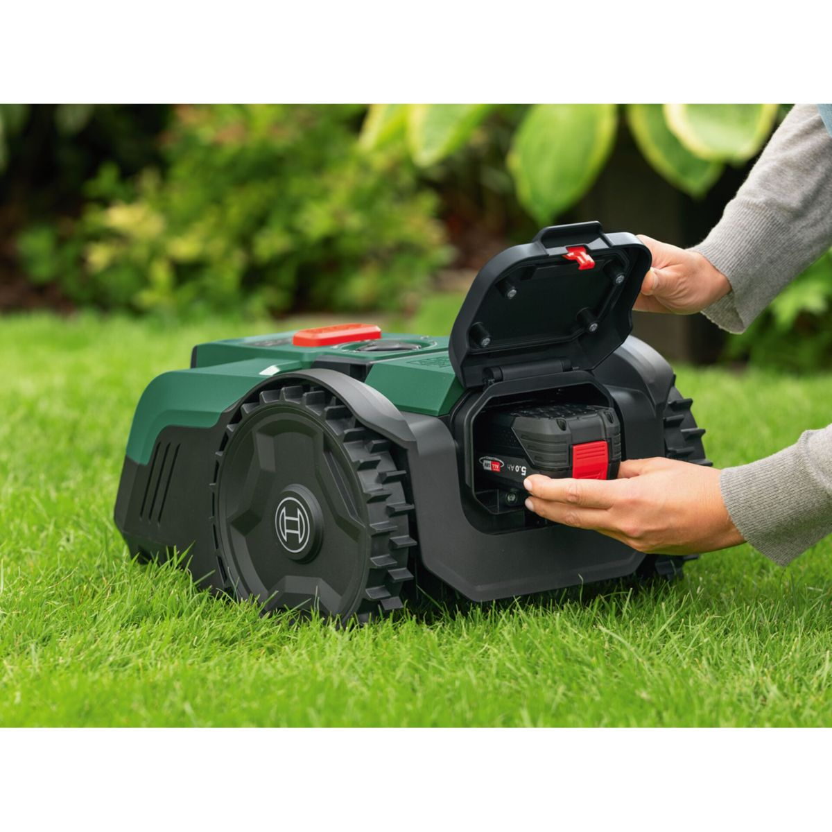 Grüner Rasenroboter mit auswechselbarem Akku in der Hand.
