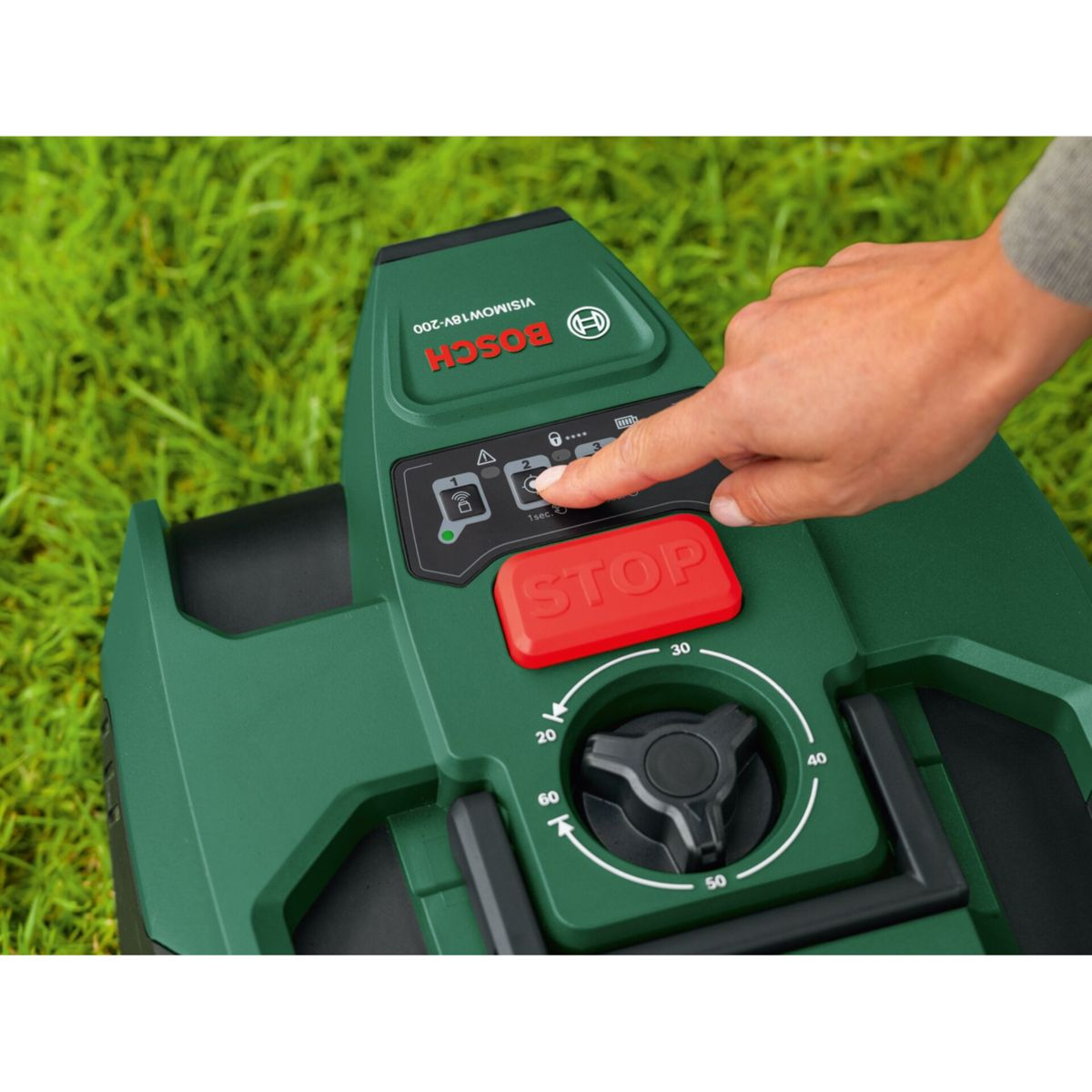 Eine Hand drückt die Stopptaste auf einem grünen Mähroboter im Gras.