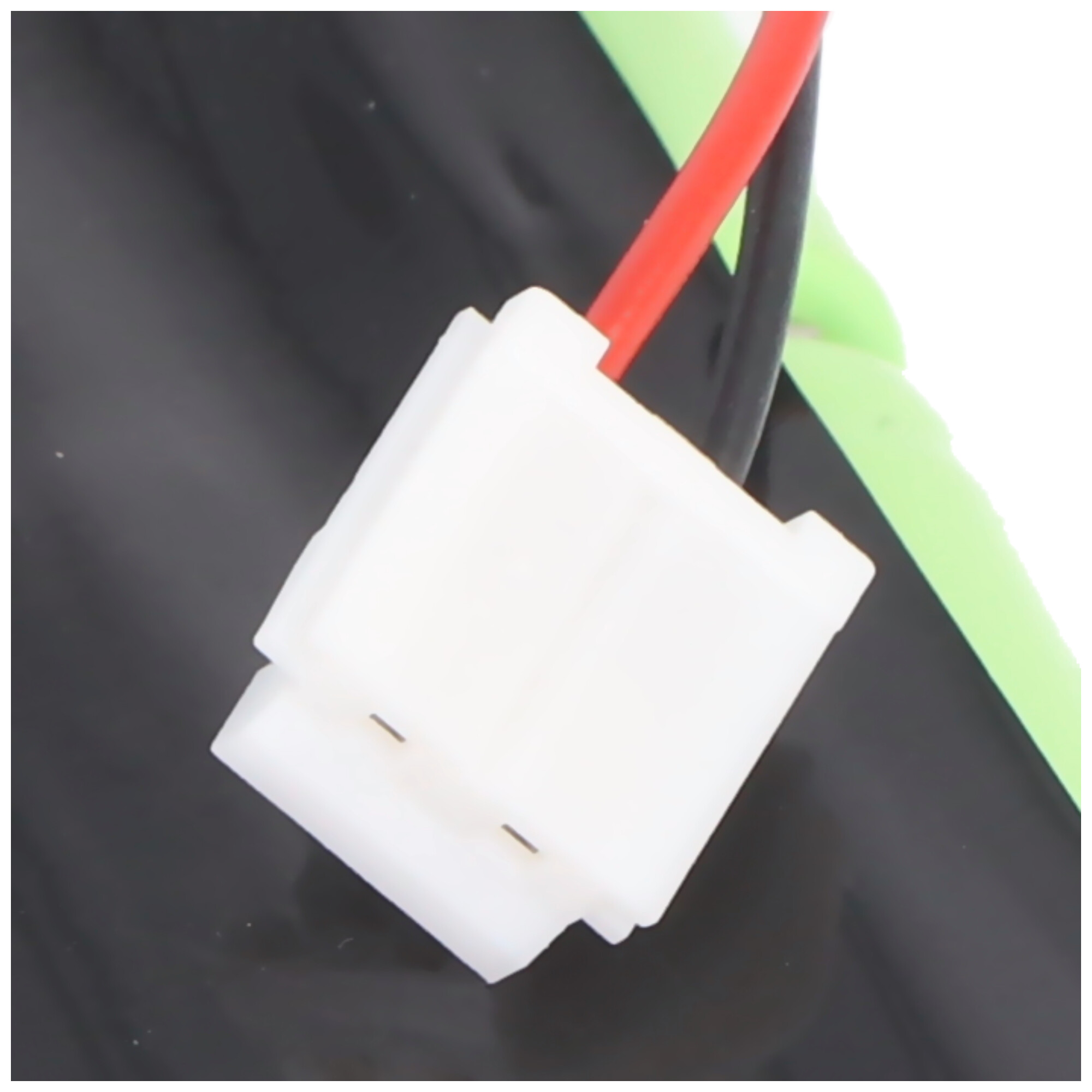 Weißer Stecker mit roten und schwarzen Kabeln auf schwarzem und grünem Hintergrund.