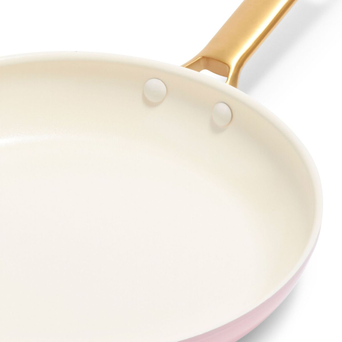 Eine Nahaufnahme einer cremefarbenen Bratpfanne mit rosa Außenseite und goldenem Griff.