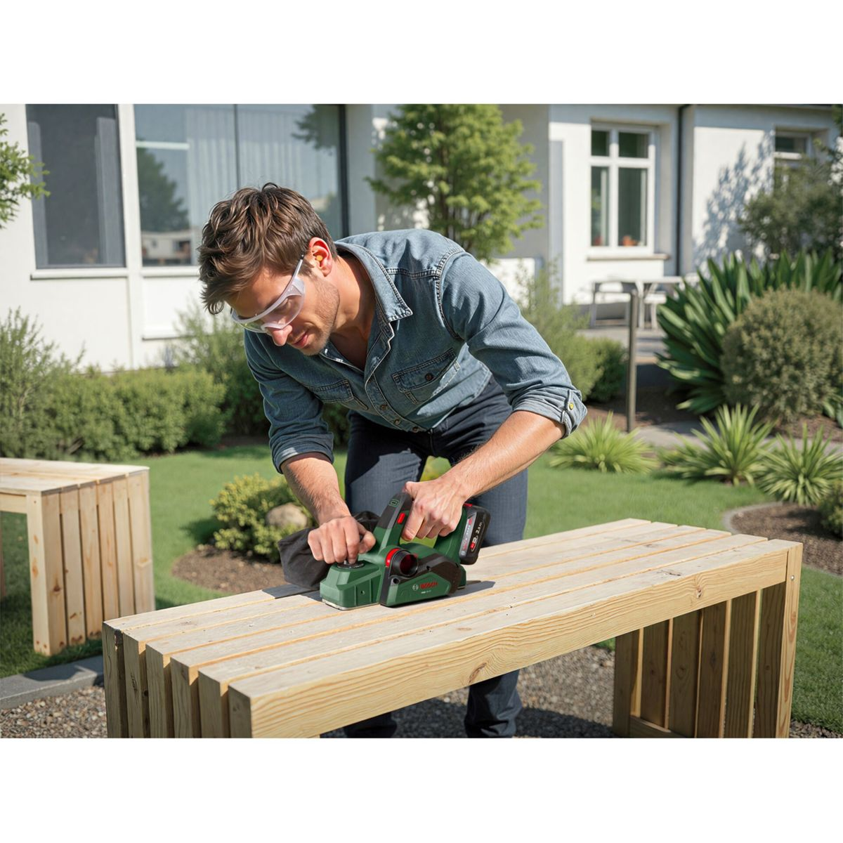 Ein Mann mit Schutzbrille bearbeitet eine Holzbank mit einem Hobel.