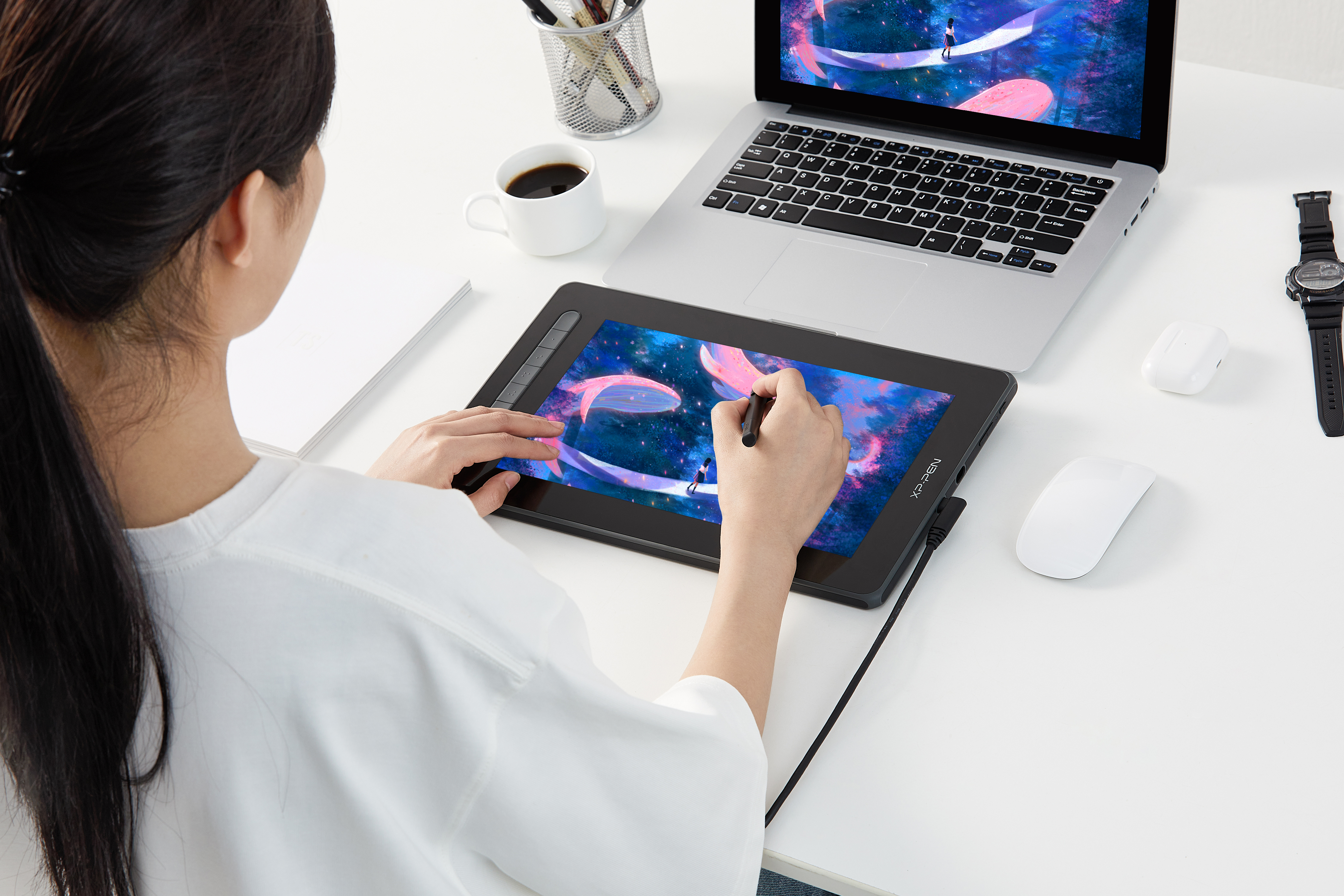 Una donna disegna su una tavoletta grafica con uno stilo, laptop e tazza di caffè nelle vicinanze.