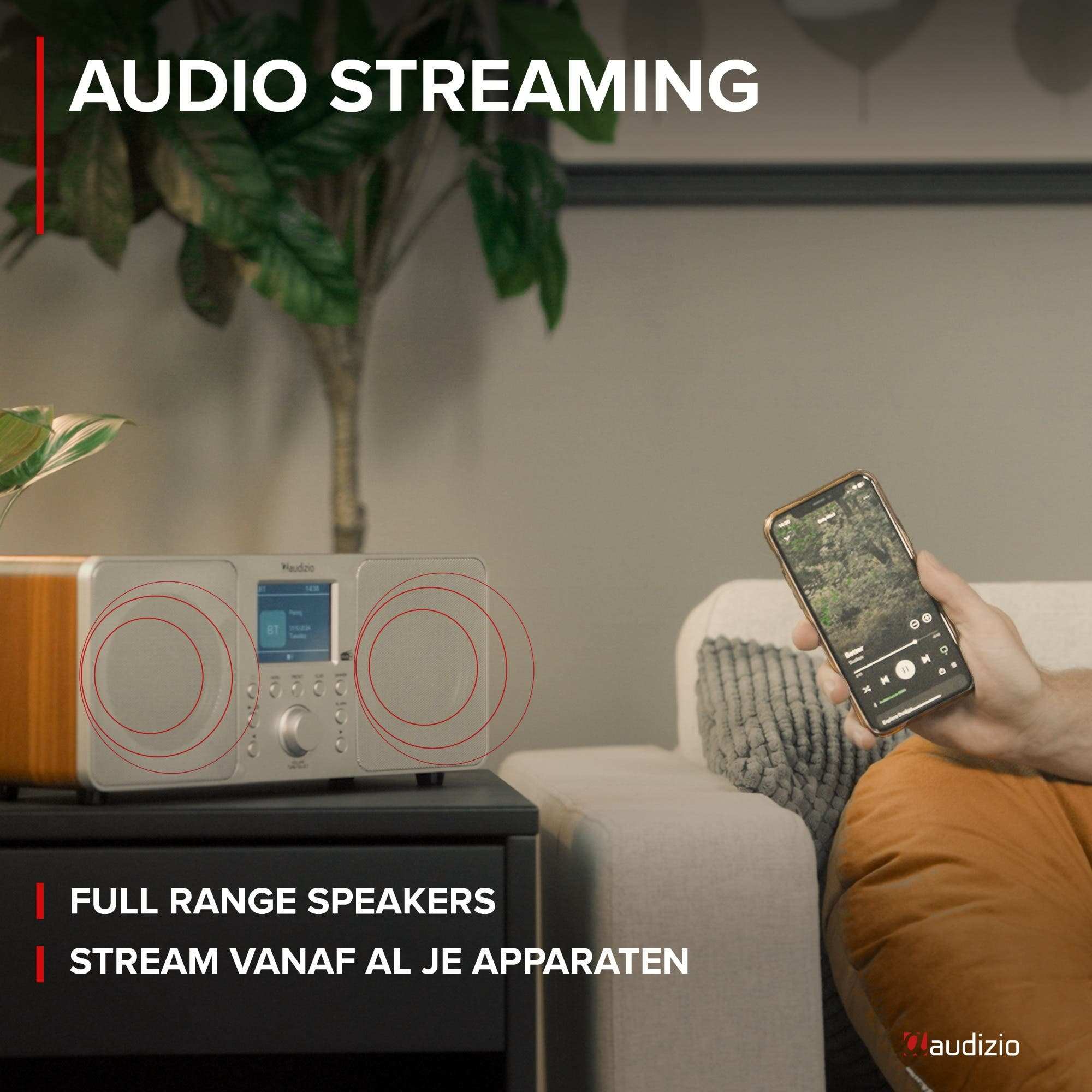 Un hombre sostiene un smartphone frente a una elegante radio Audizio con altavoces.