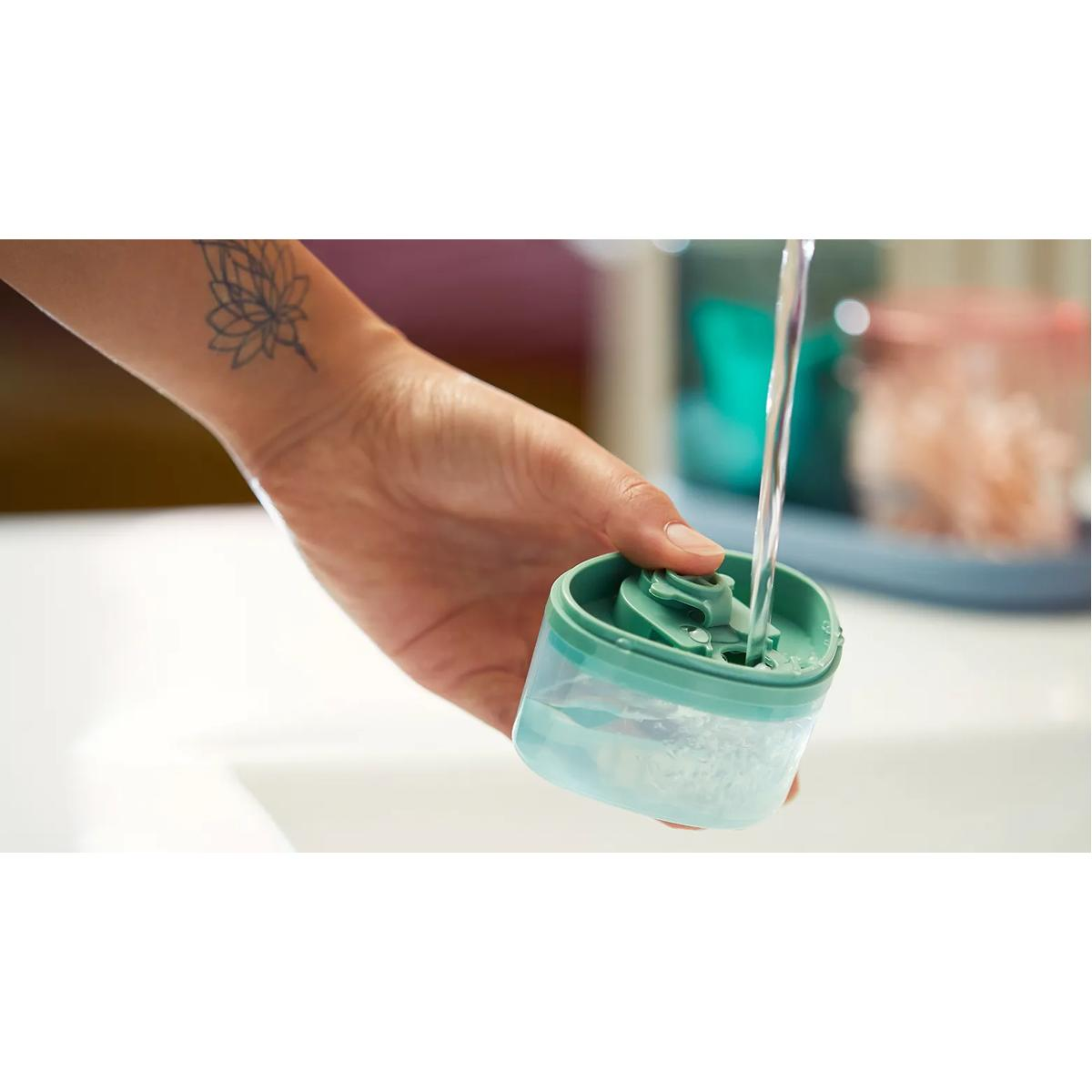 Wasser fließt in einen kleinen Behälter, der von einer Hand gehalten wird.