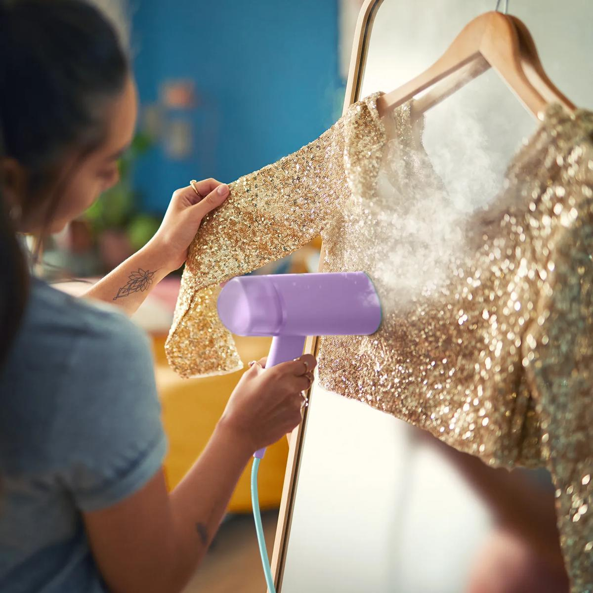 Een vrouw stoomt een gouden pailletten top met een handstomer.