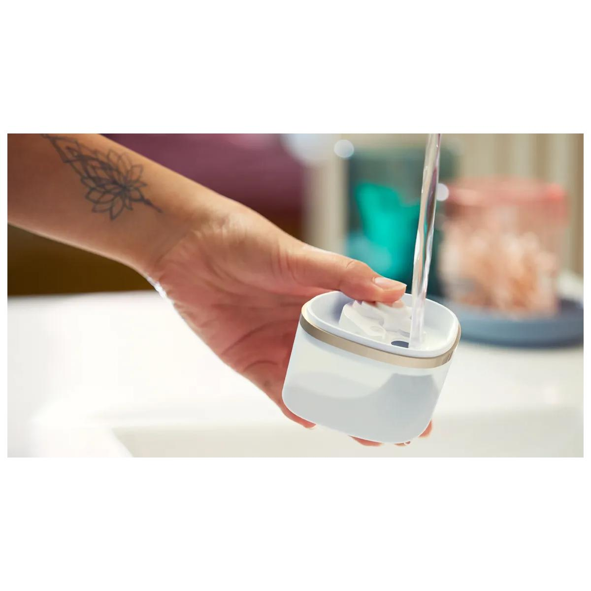 Wasser fließt in einen kleinen Behälter, den eine Hand mit Tattoo hält.