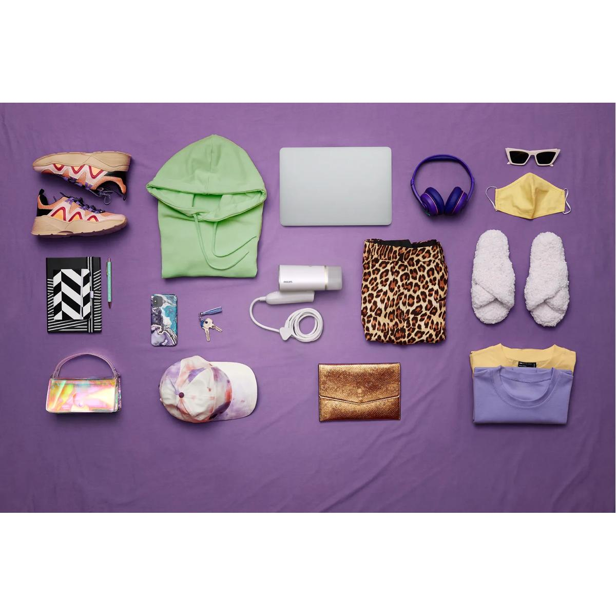 Blick auf einen flachen Lay von Kleidung und Accessoires auf lila Stoff.