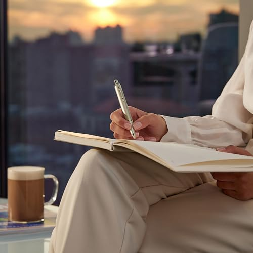 Eine Person schreibt in ein Notizbuch, eine Tasse Kaffee daneben, Sonnenuntergang im Hintergrund.