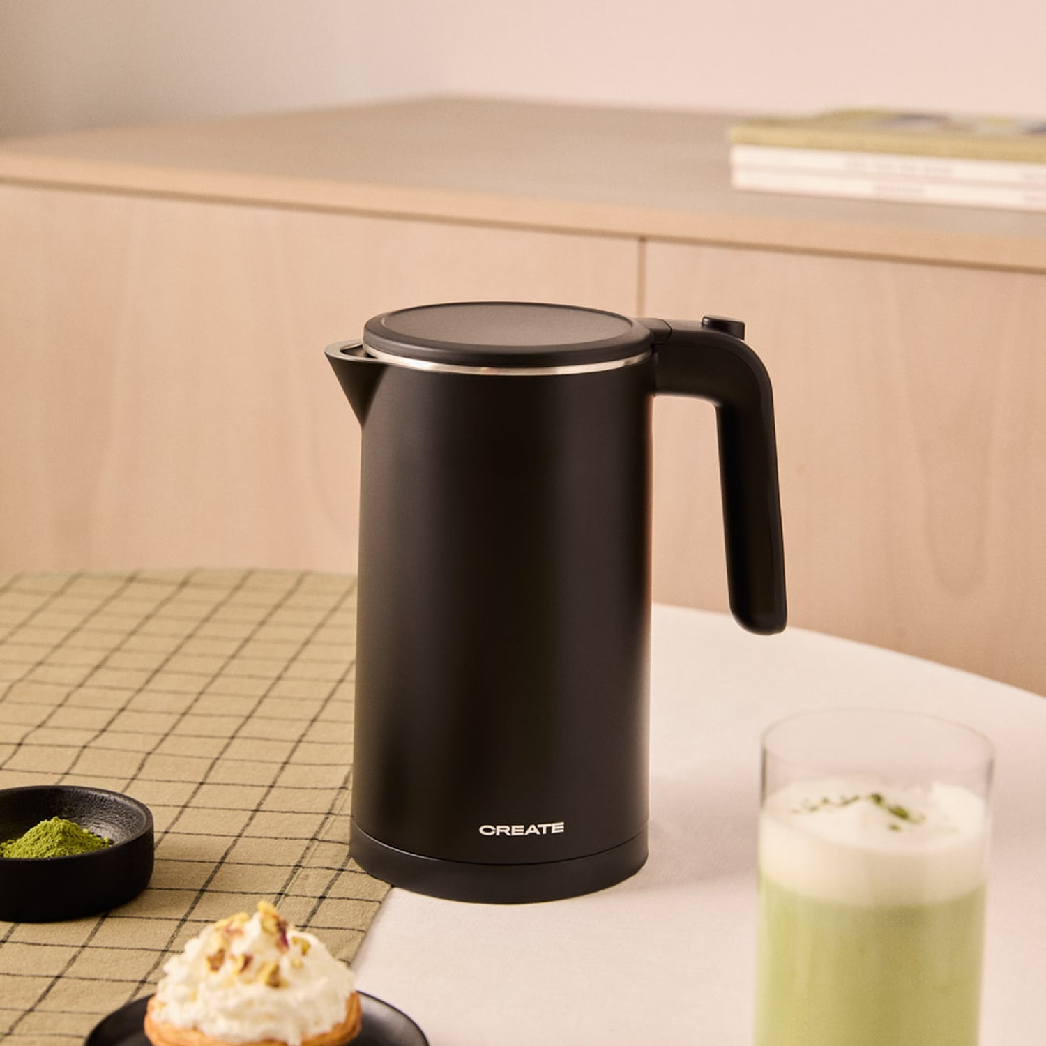 Un hervidor negro con un vaso de bebida y polvo de matcha.