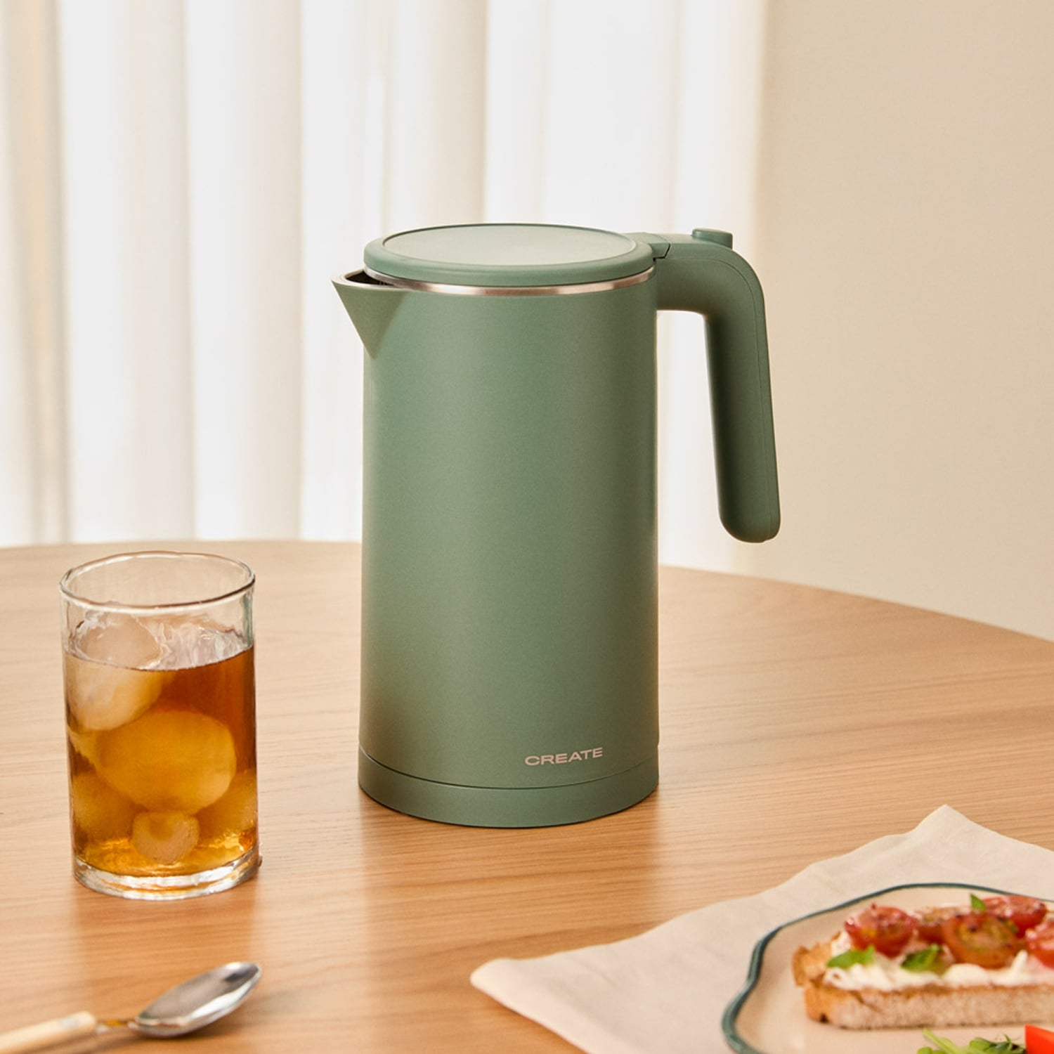Un hervidor verde junto a un vaso de té helado sobre una mesa de madera.