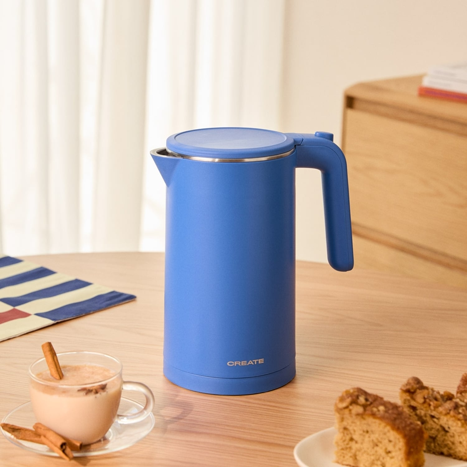 Un hervidor azul sobre una mesa de madera con una taza de té y pastel.